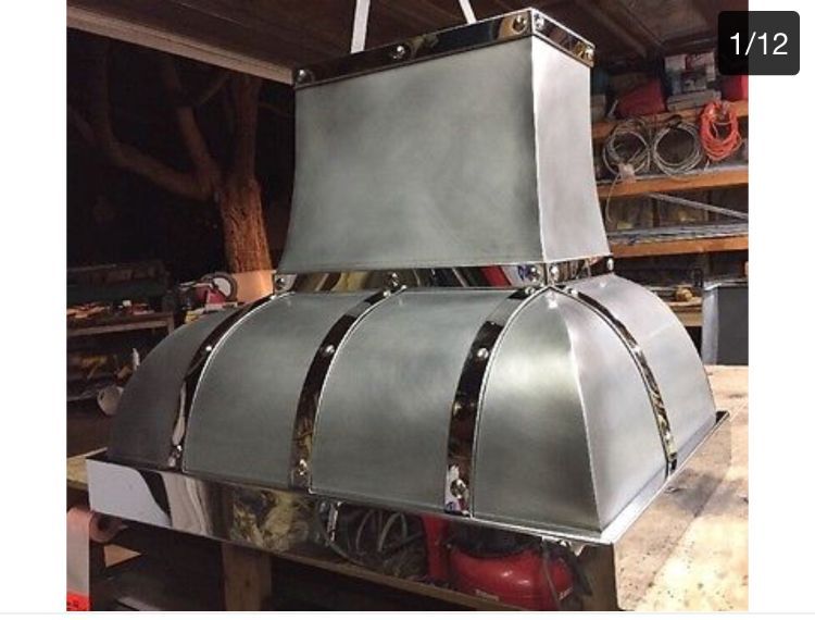 Custom stainless steel ventilation hood in a workshop, with curved metal panels and a square chimney top