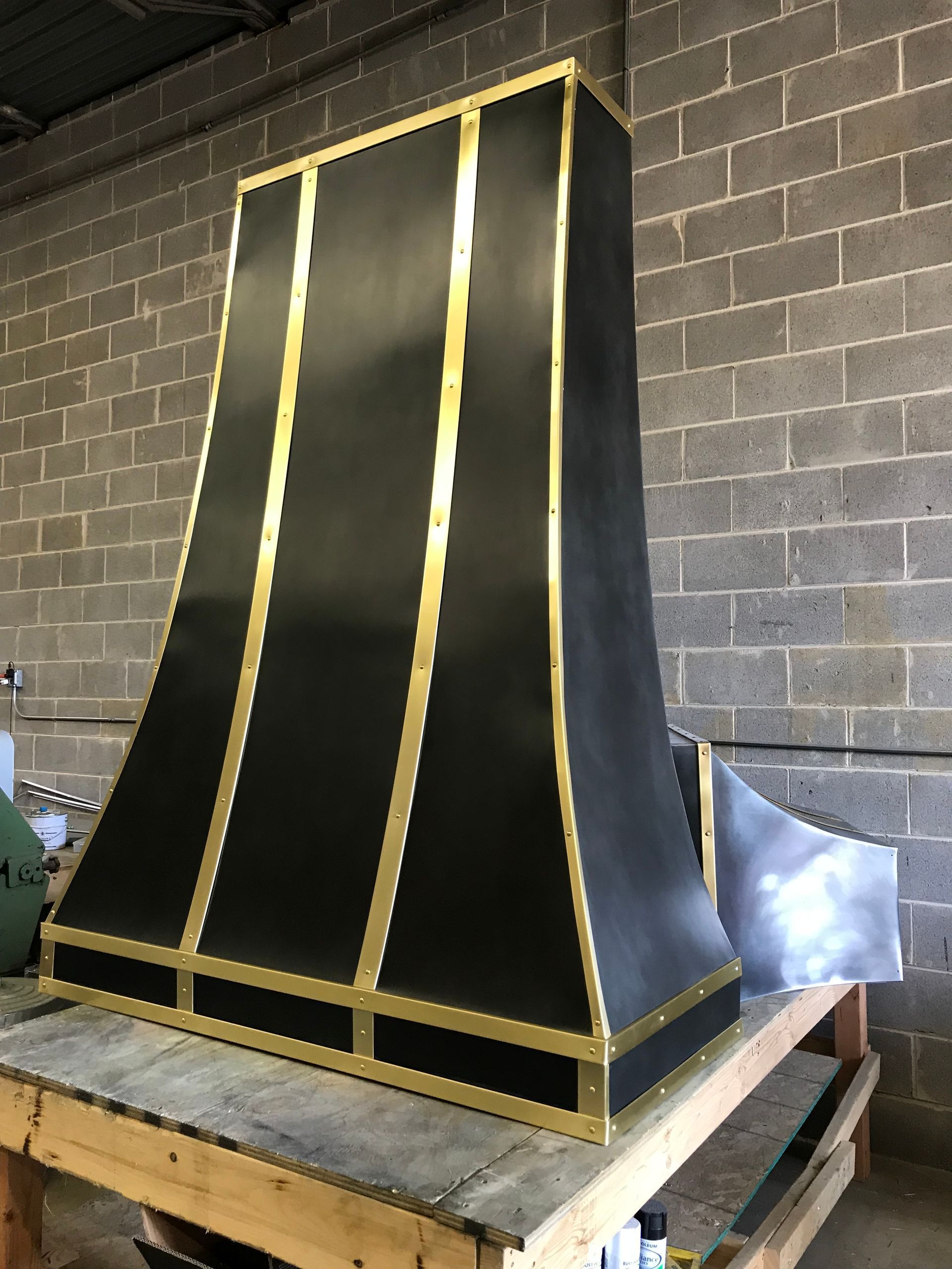 Large black metal enclosure with gold trim on a workbench in a workshop.