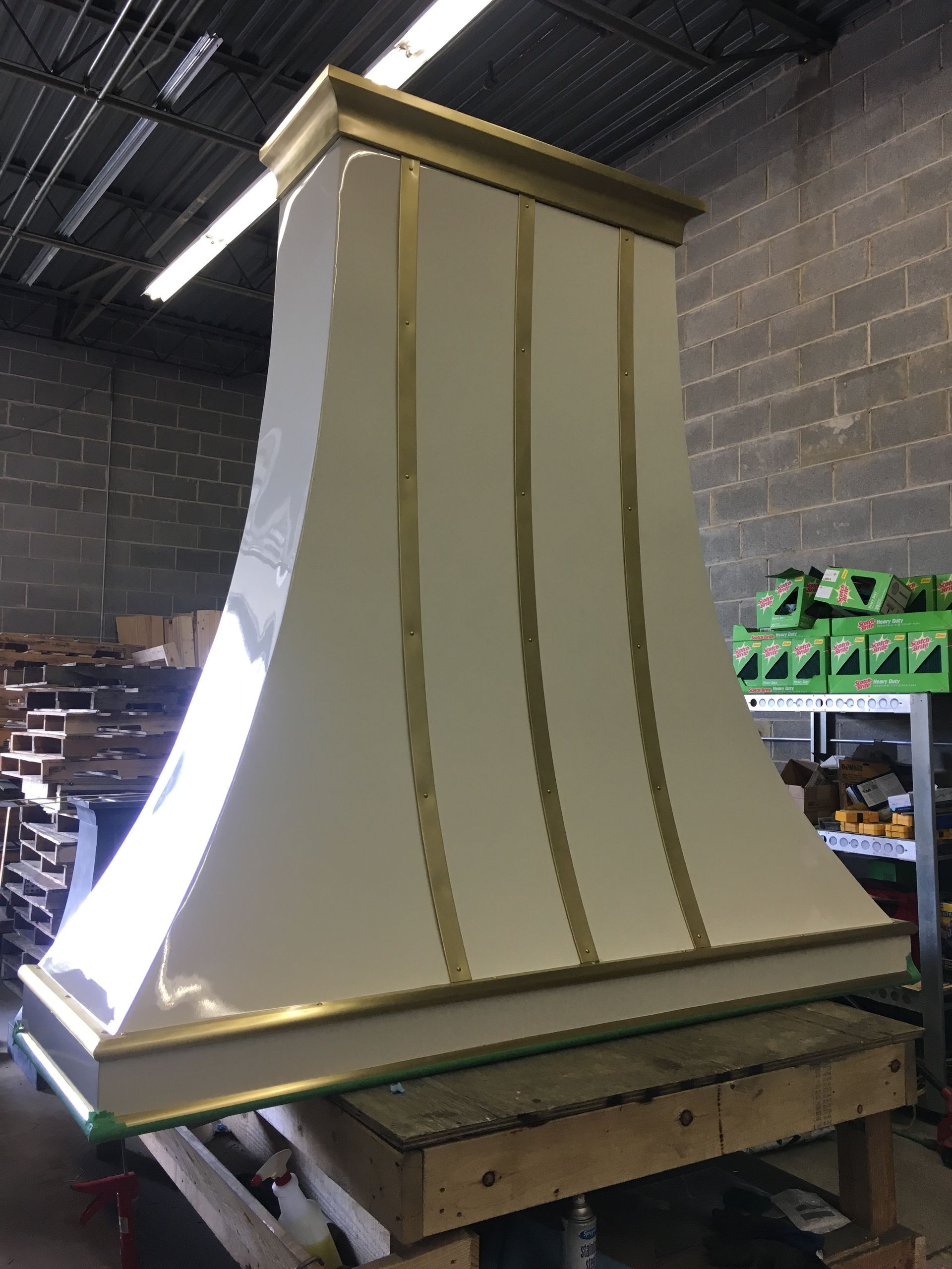 Large cream-colored tapered cabinet or chimney hood under construction in a workshop, with exposed wooden supports.