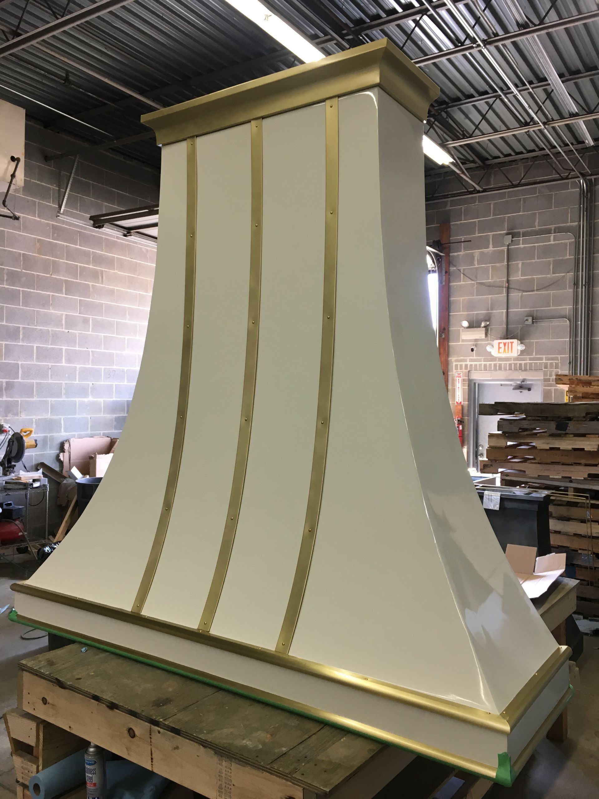 Tall cream-colored decorative column or vent hood with gold trim in a workshop, standing on a wooden pallet