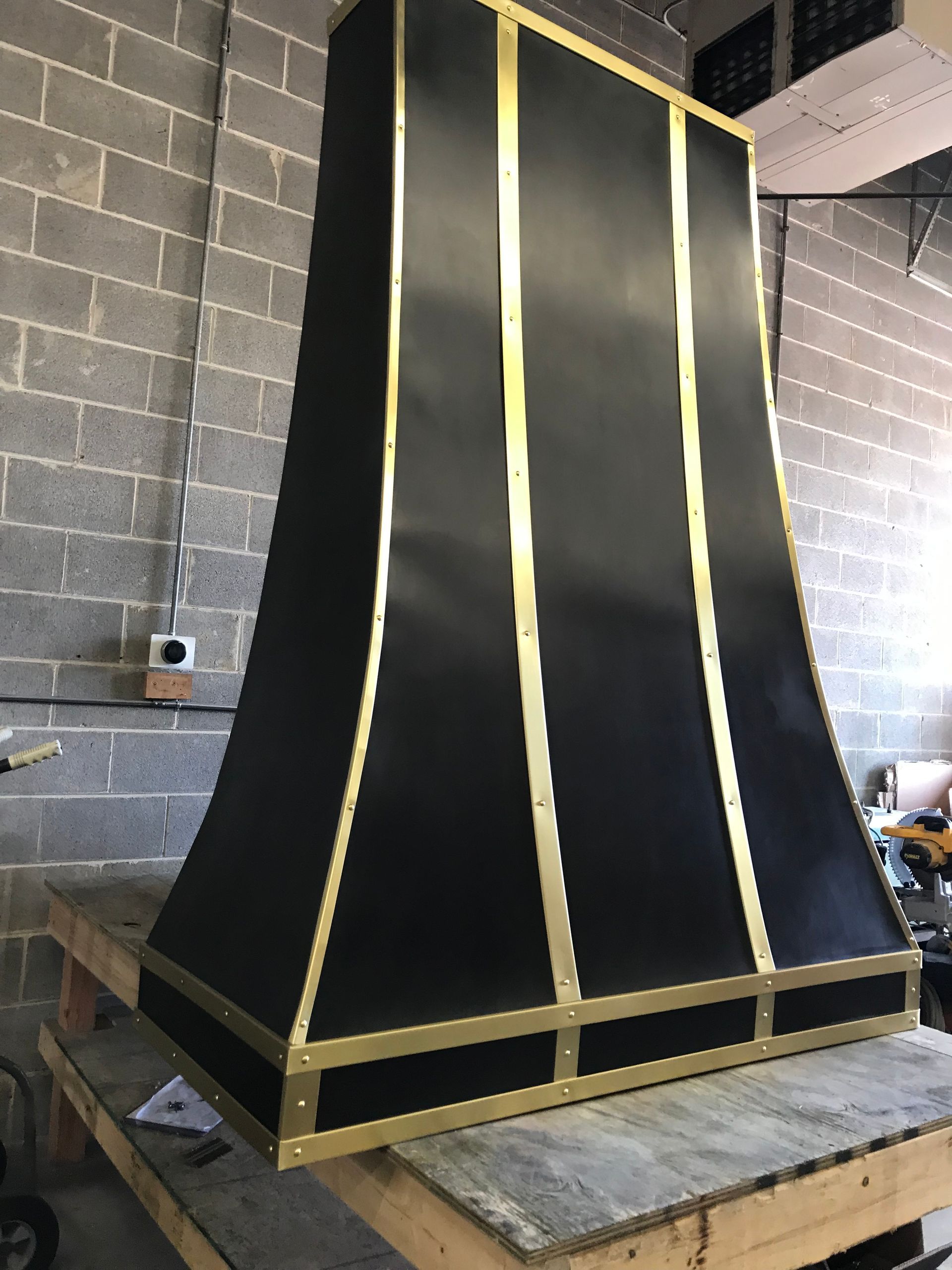 Tall black hooded structure with gold trim, standing on a wooden platform in a workshop-like room.