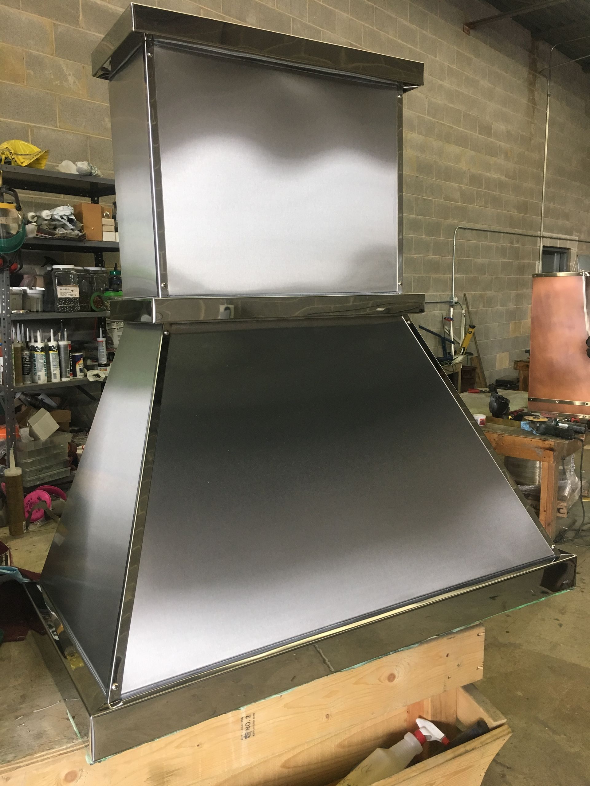 Large metal vent hood assembly with sloped stainless-steel panels in a workshop.