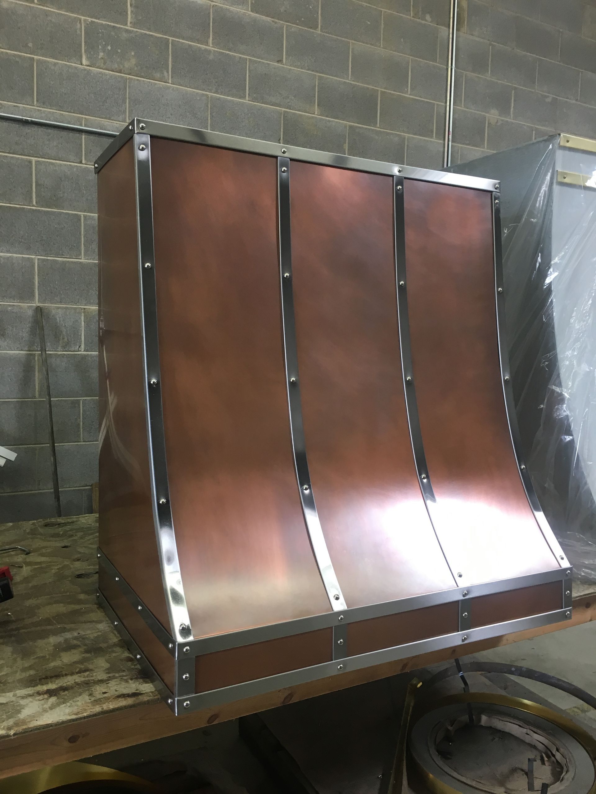 Copper-colored metal hood with three curved panels in an industrial workshop