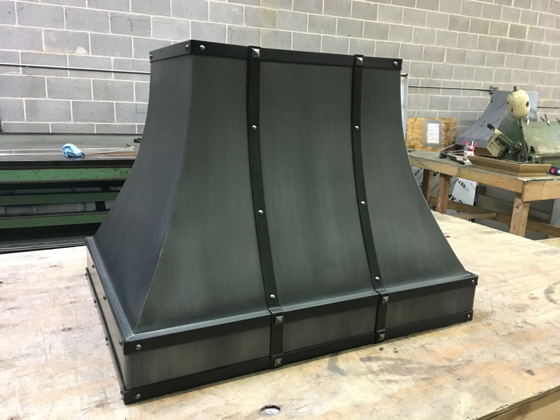 Black metal vent hood on a workbench in a workshop, with a cinderblock wall in the background