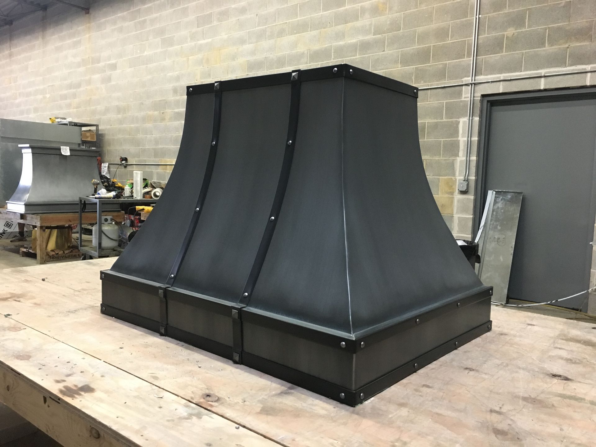 Black metal industrial hood or vent on a wooden platform in a workshop