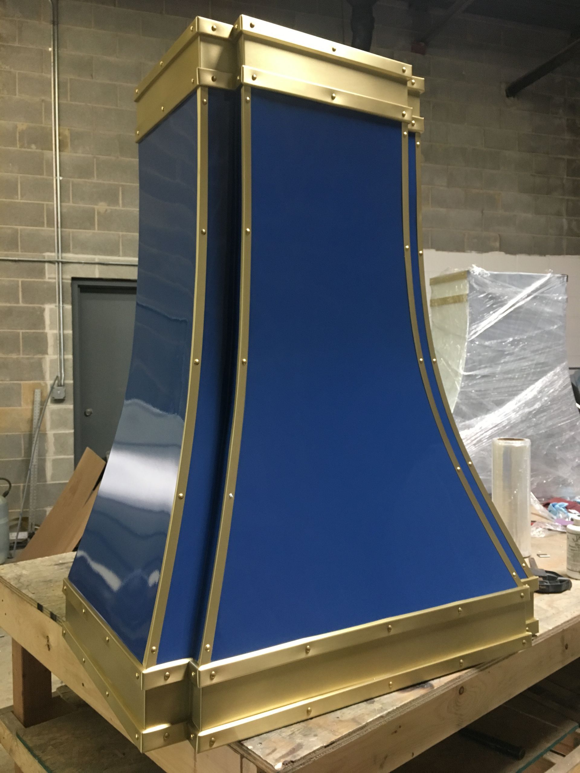 Blue-and-gold ornate structure on a wooden crate in a workshop, possibly a decorative panel or casing