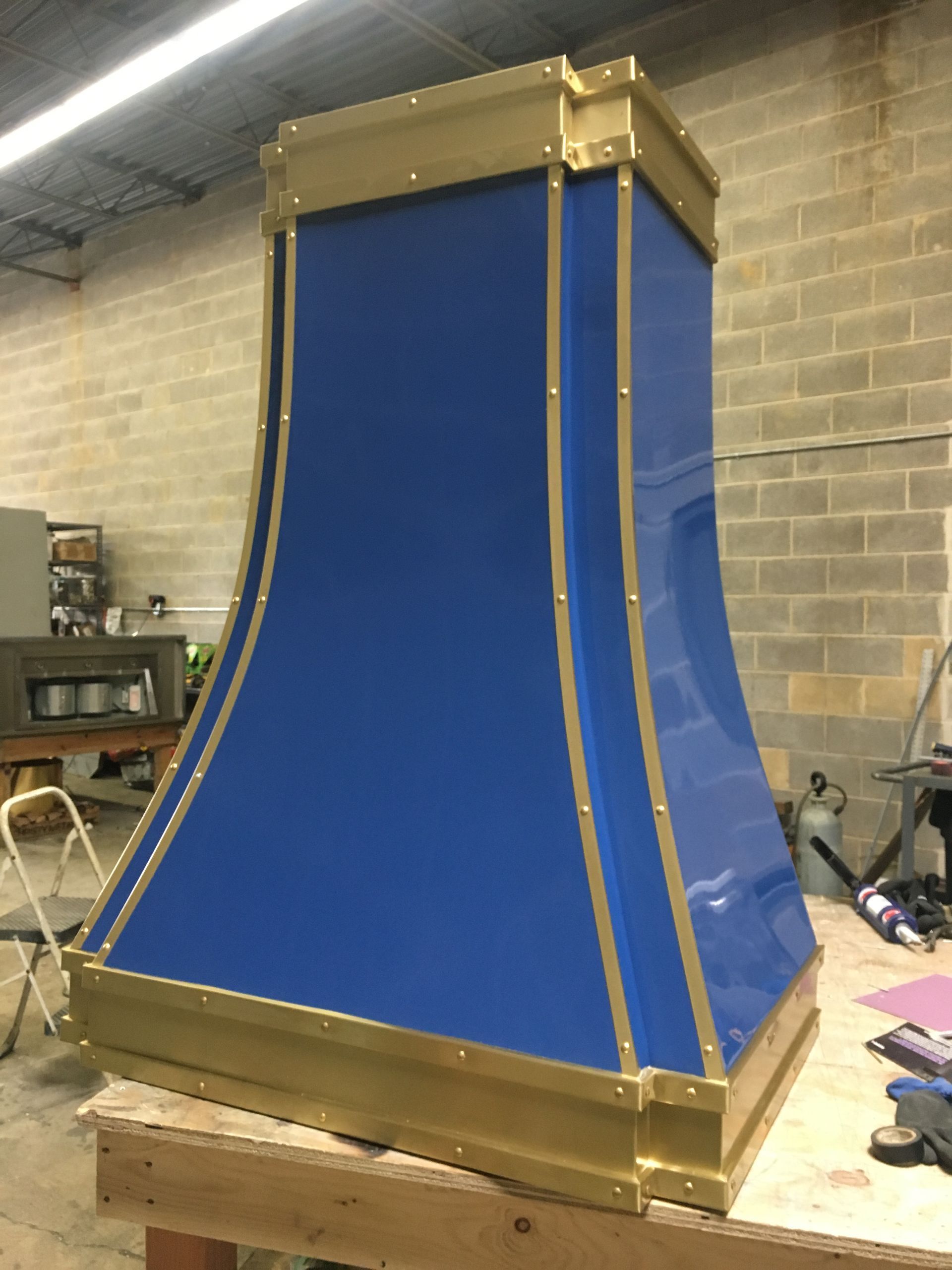 Blue fabric draped over a curved wooden frame in a workshop, resembling a prototype chute or slide.