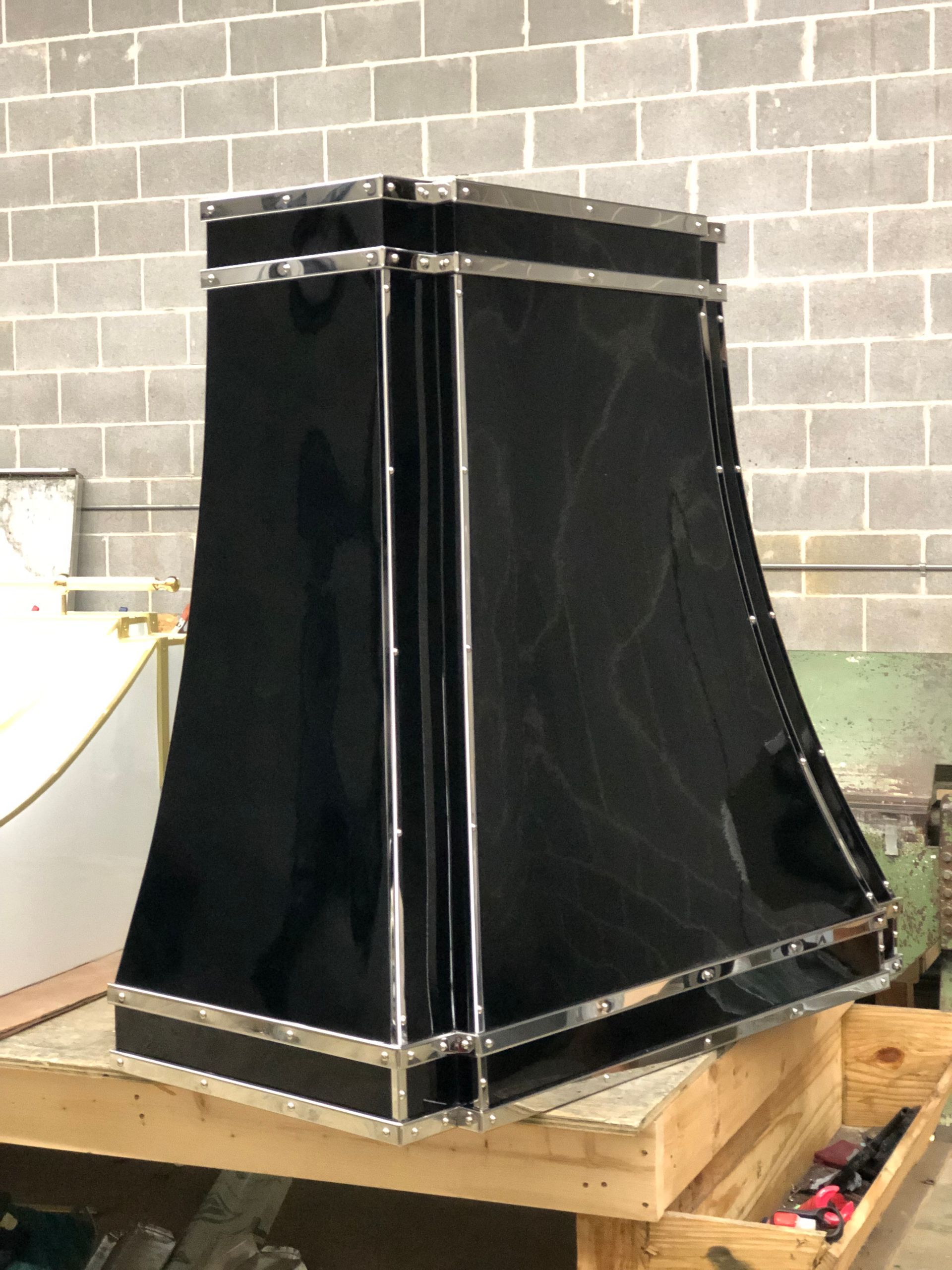 Black fabric industrial vent hood on a wooden pallet in a workshop, against a cinder block wall