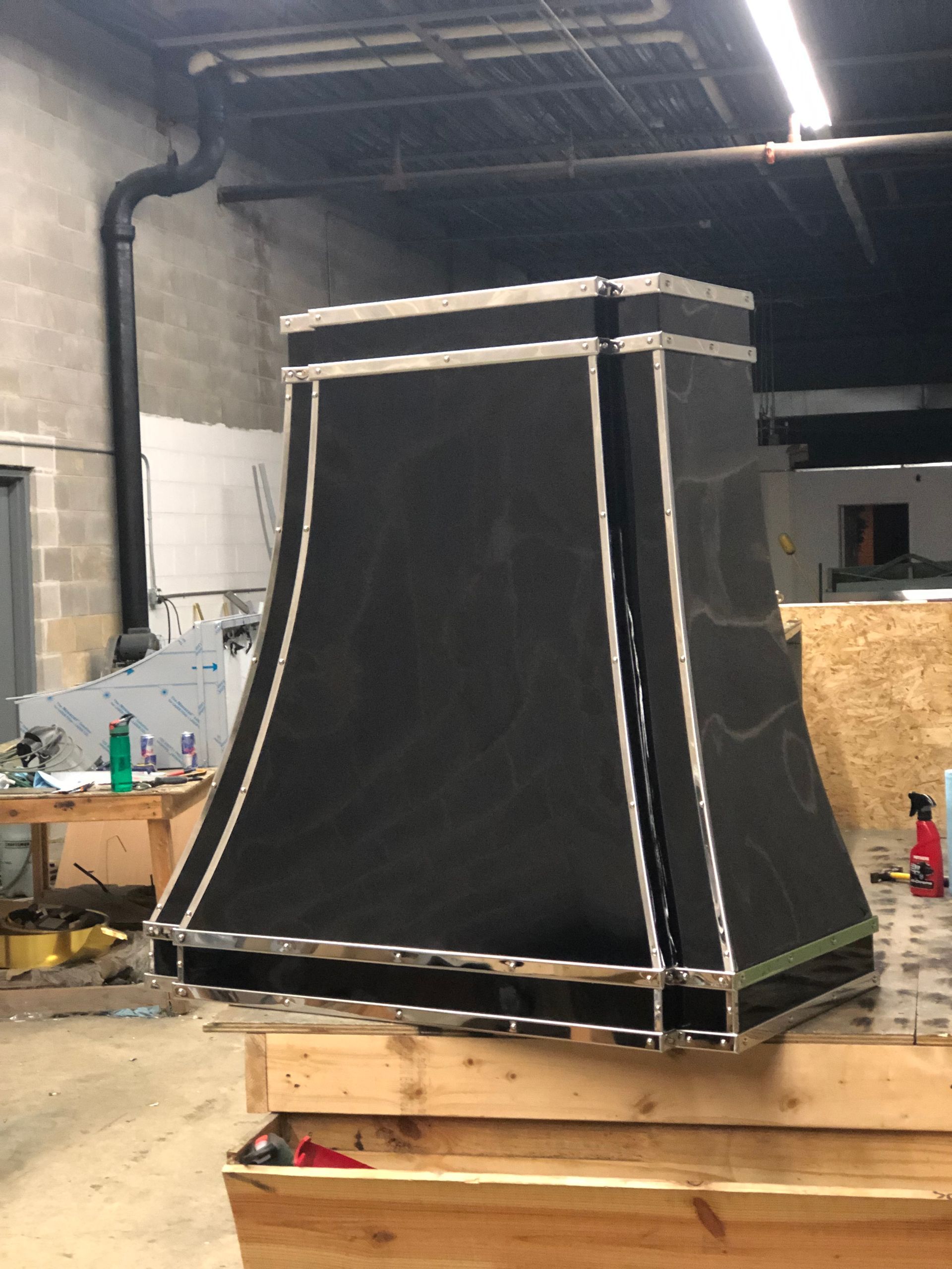 Large black fabric structure with white trim on a wooden pallet inside a workshop