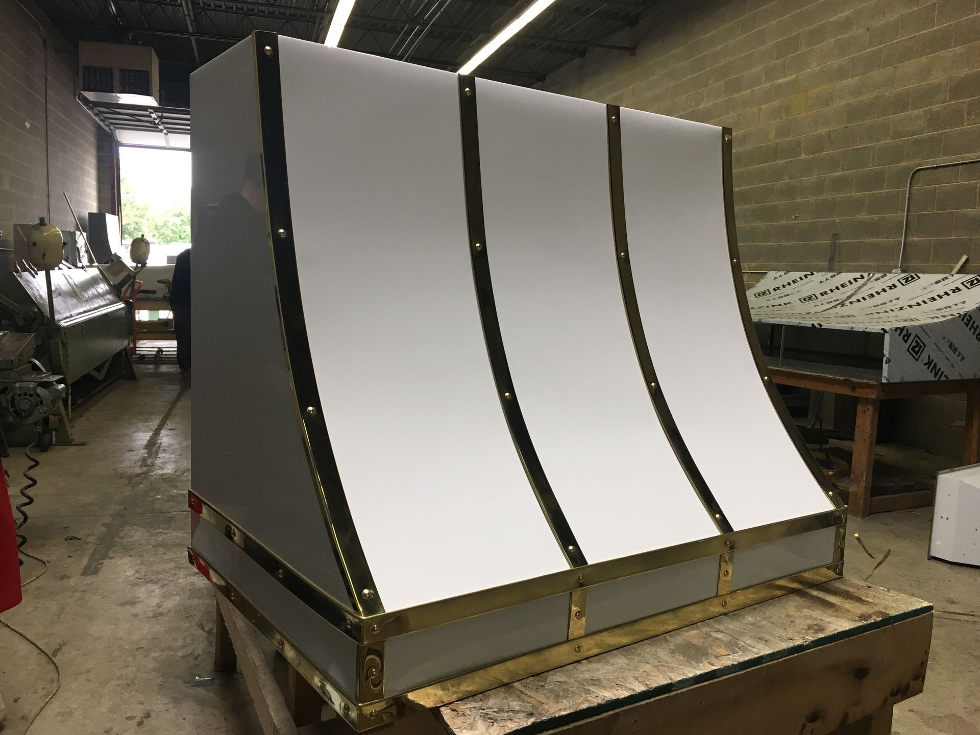 Three large curved white metal panels on a wooden pallet in a workshop