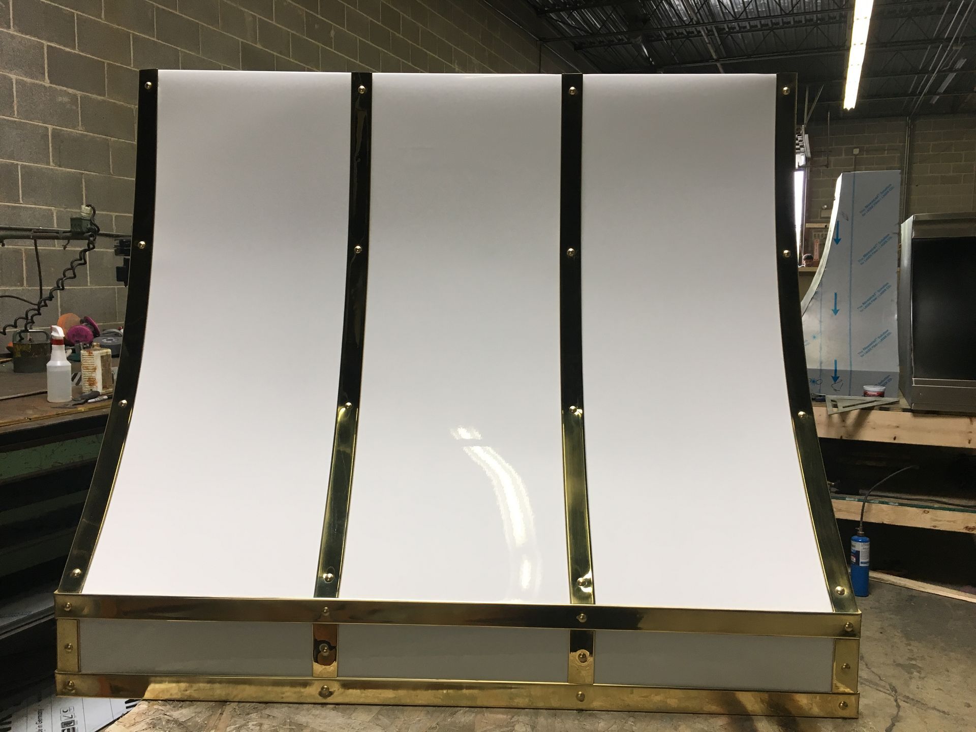 Three glossy white curved panels mounted on a wooden frame in a workshop.