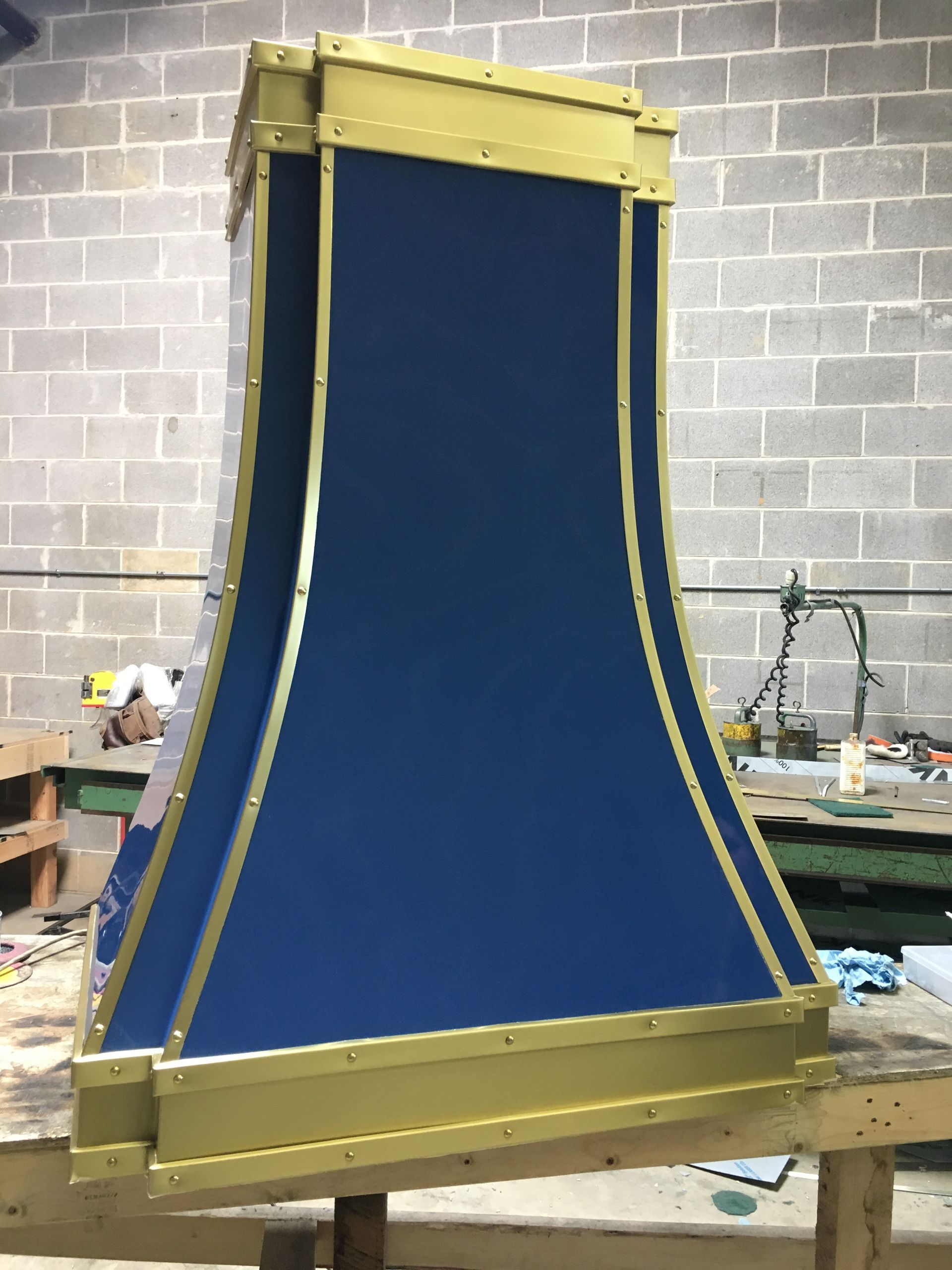 Large blue fabric panel with gold frame in a workshop against a cinderblock wall