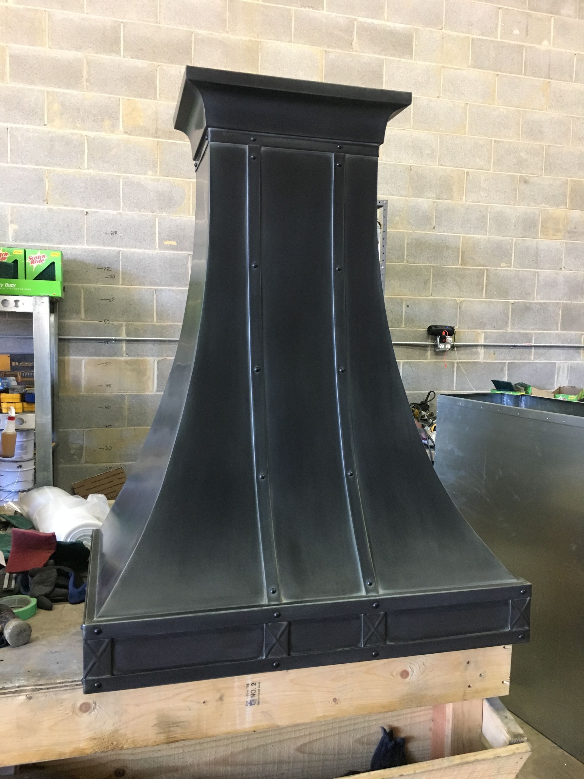 Black metal chimney hood on a wooden pallet in a workshop