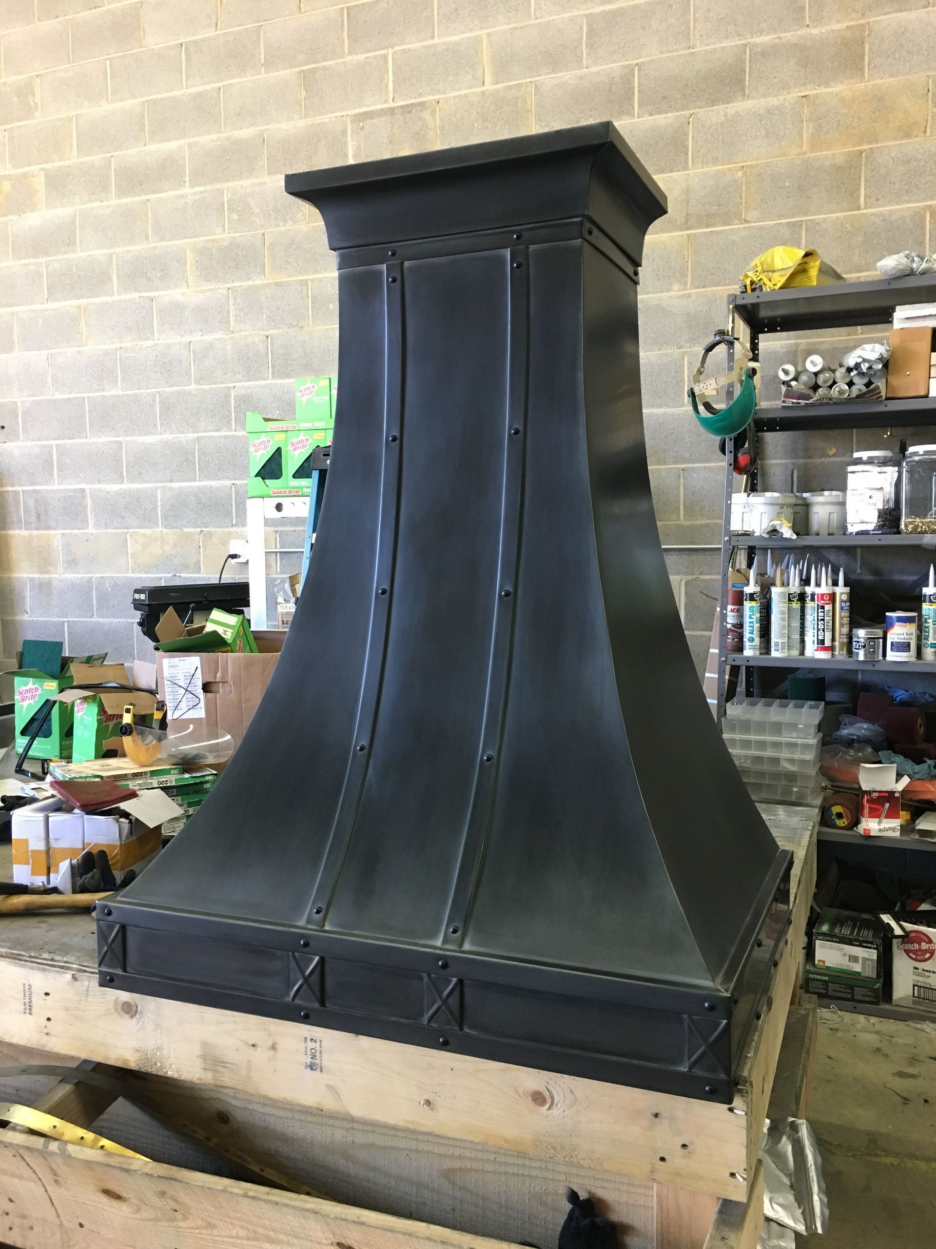 Black range hood being installed in a workshop, with shelves and tools in the background