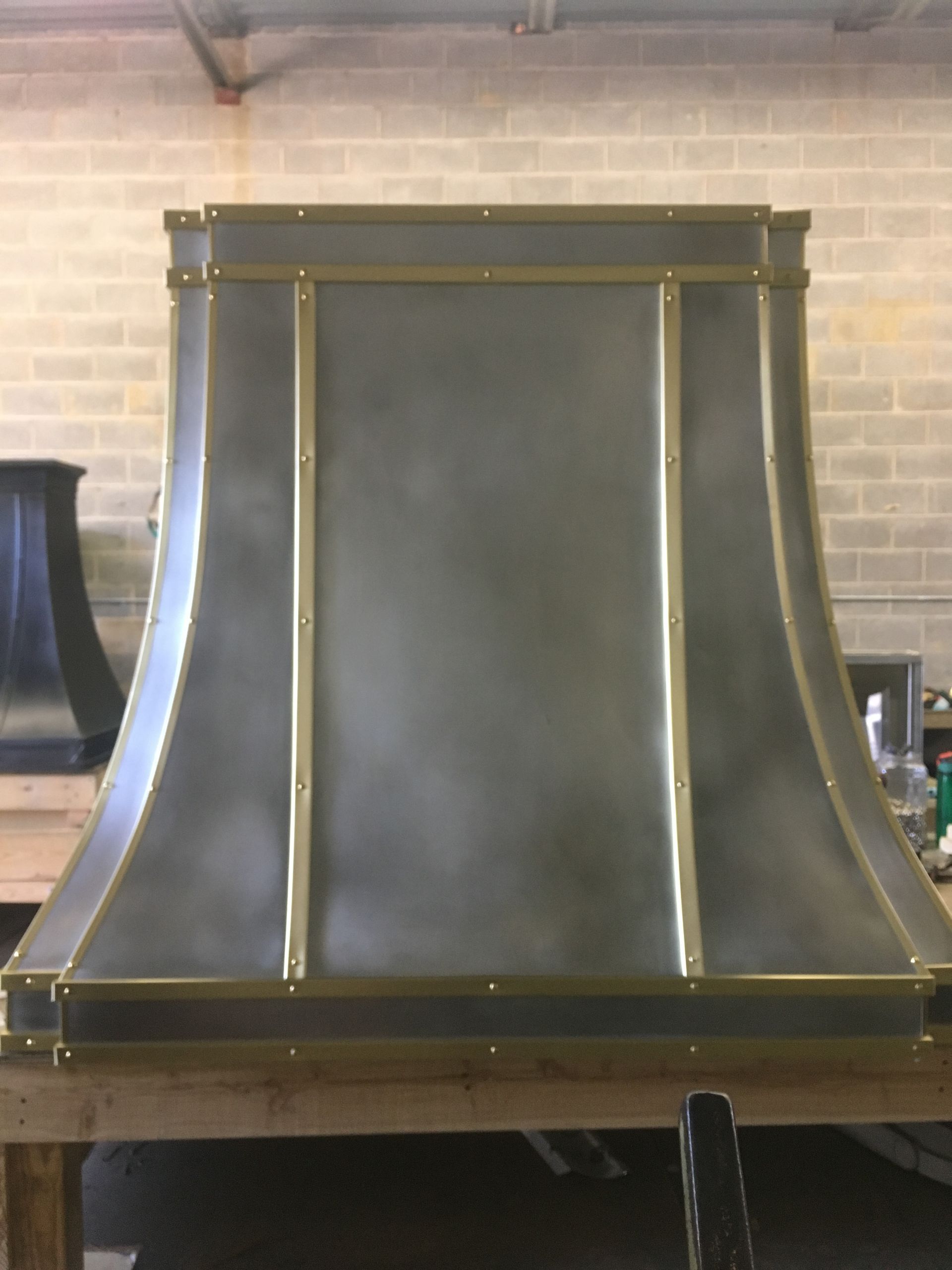 Black metal chimney hood with gold trim against a brick wall