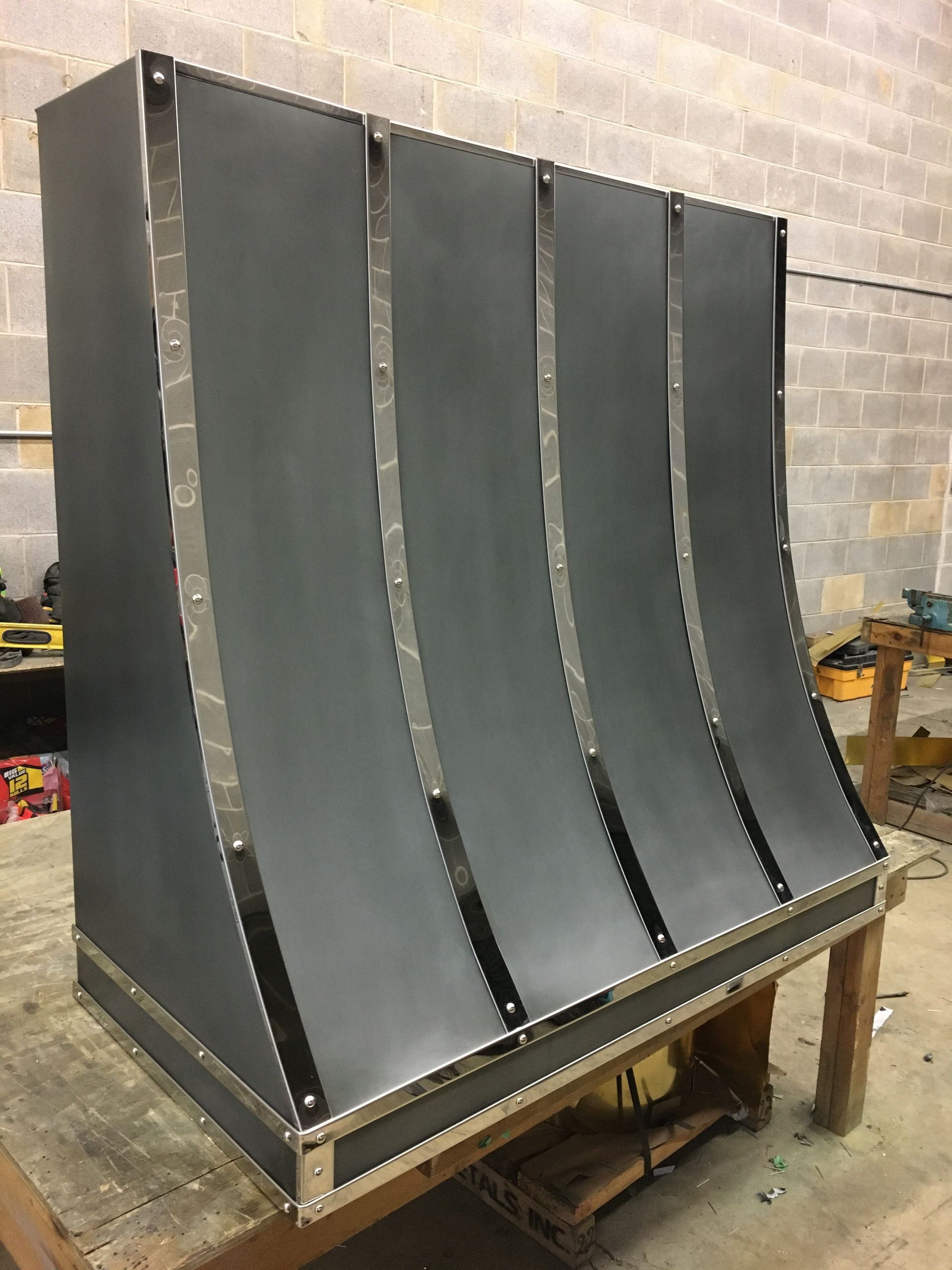 Black curved metal panel assembly on a wooden pallet in a workshop.