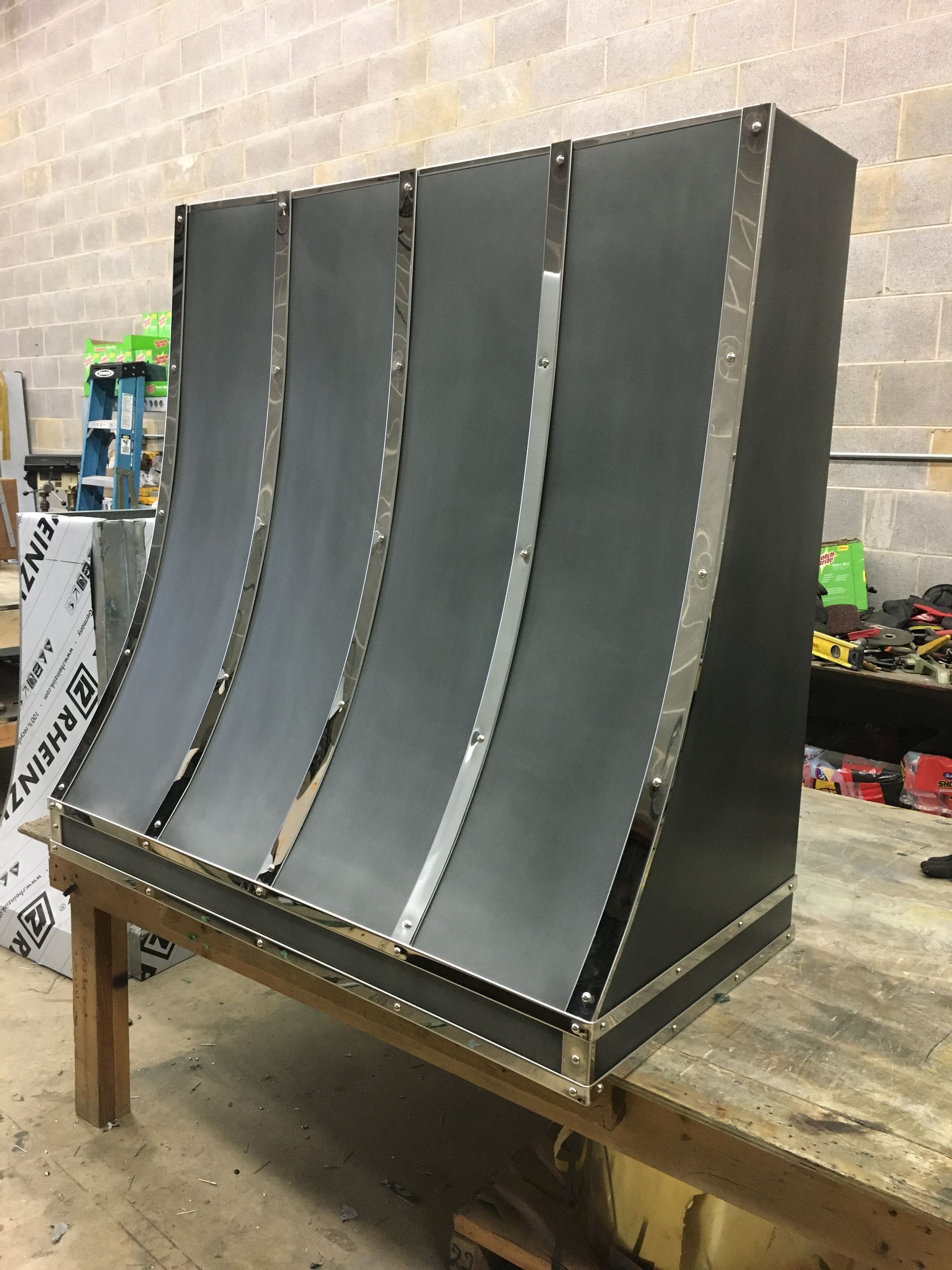 Large dark gray curved metal structure on a workbench in a workshop under construction.