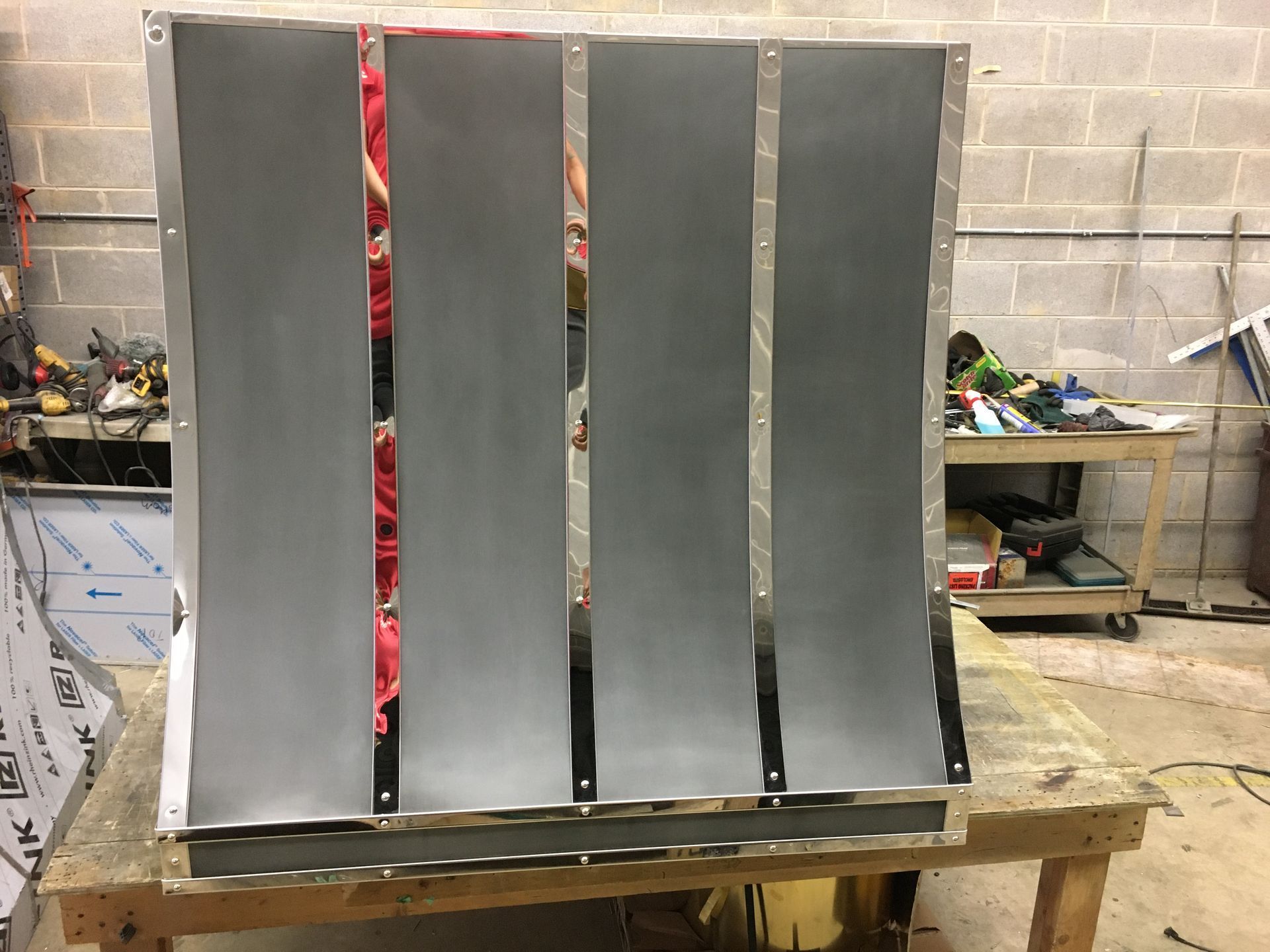 Four gray vertical panels mounted on a wooden pallet in a workshop, with a red strip visible behind them