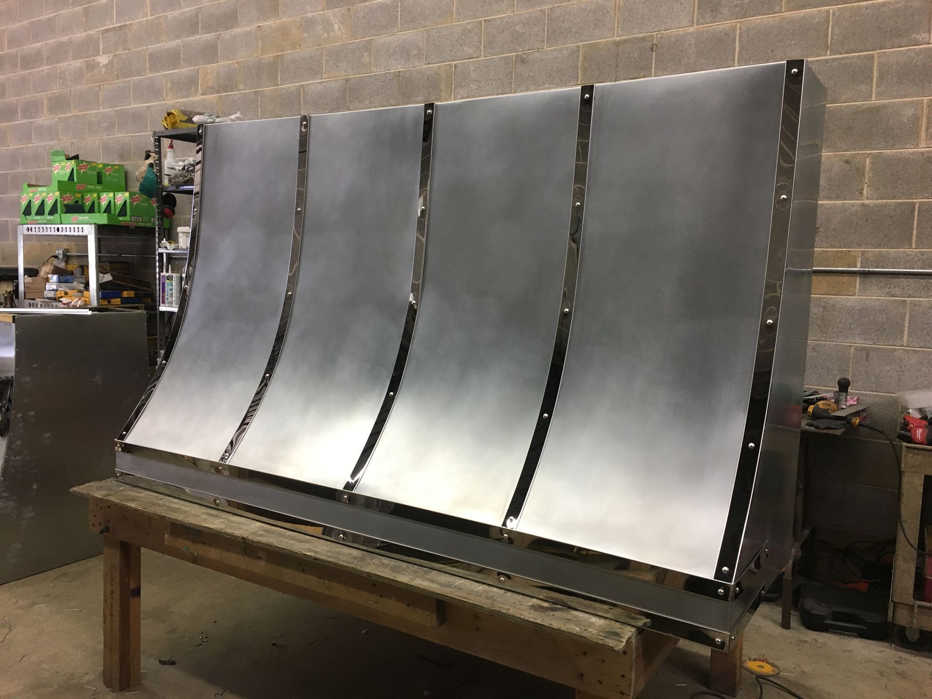 Curved metal sheet panels on a workbench in a workshop, with equipment in the background