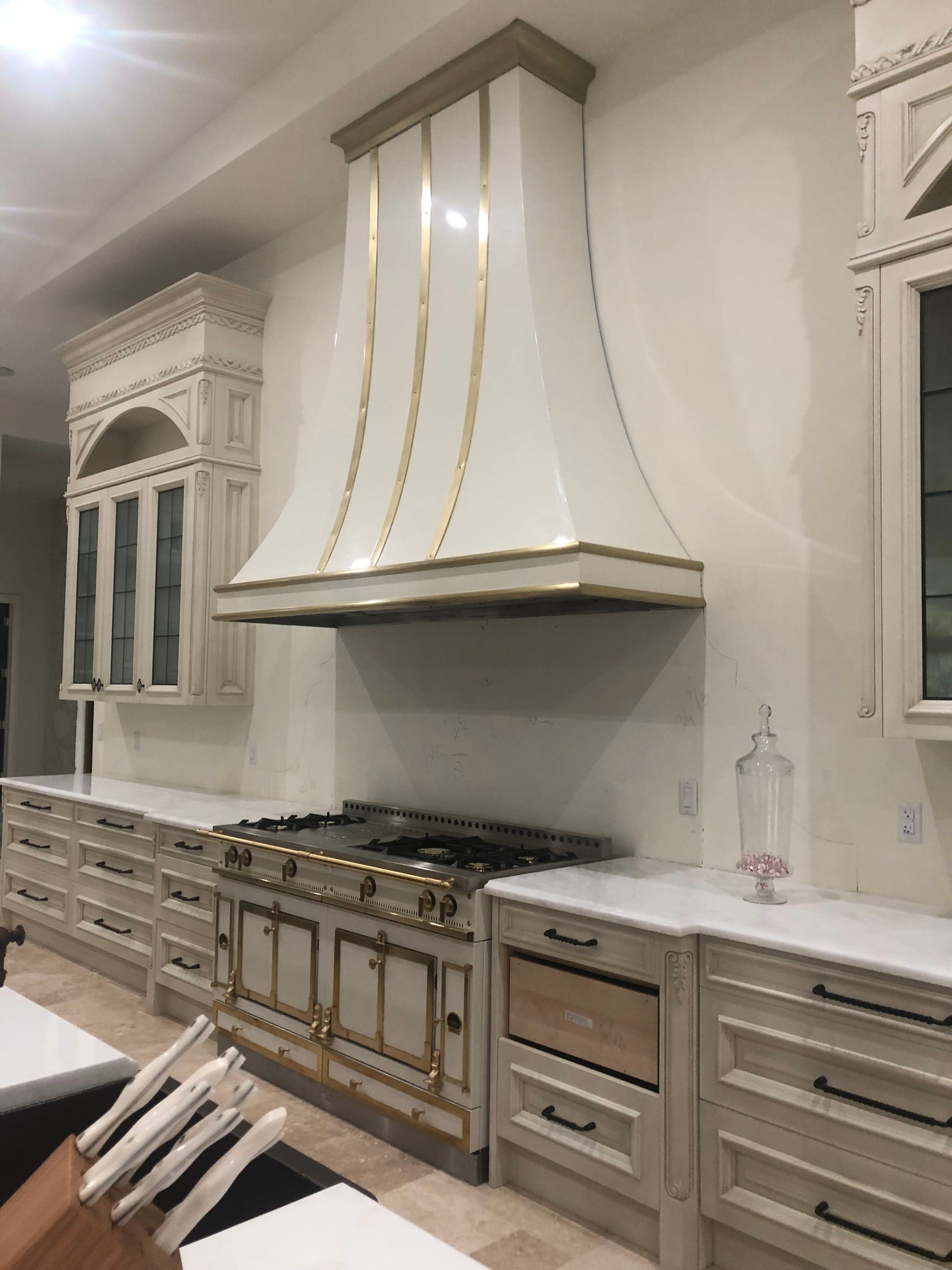 Elegant white kitchen with ornate cabinets, marble countertops, and a large range hood over a gas stove