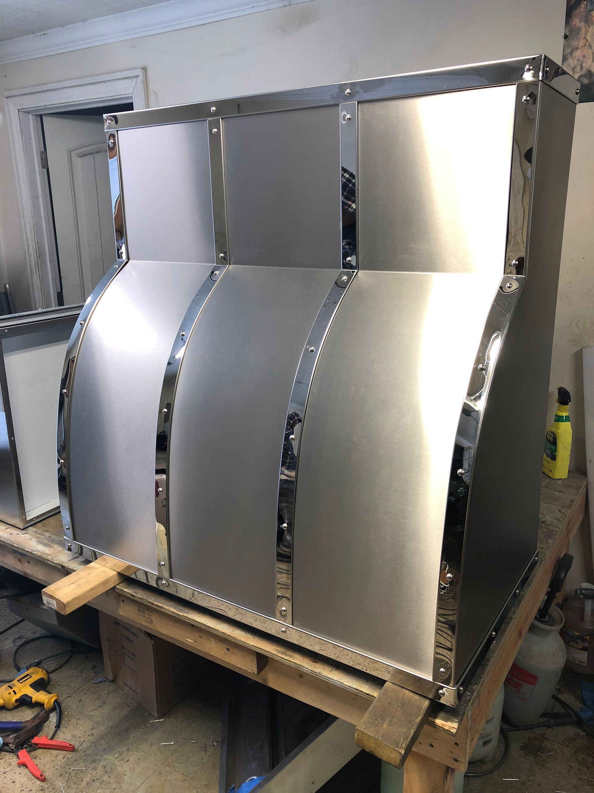 Three curved metal panels mounted on a wooden frame in a workshop.