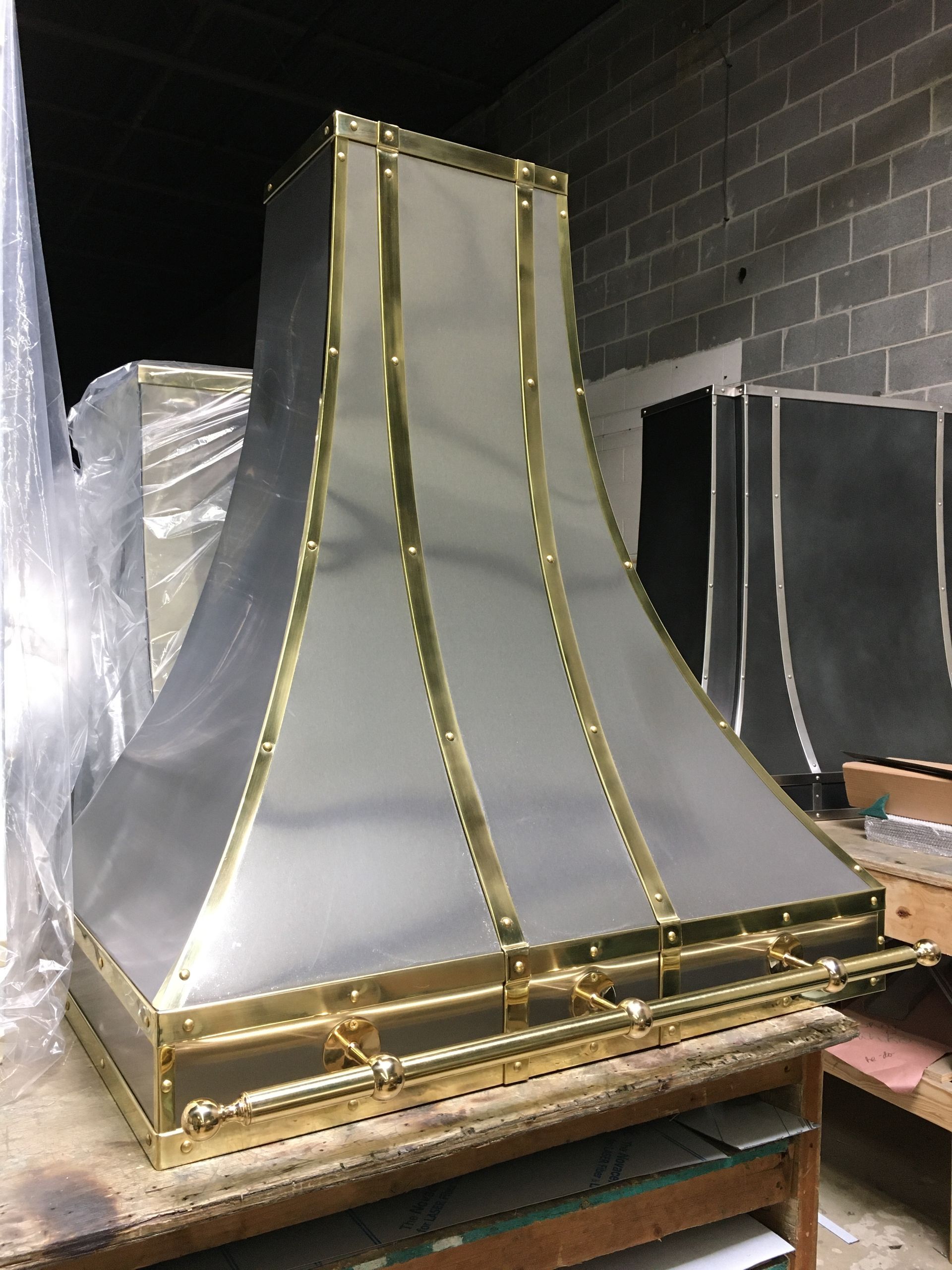 Metal kitchen hood duct with gold trim sitting on a wooden pallet in a storage area