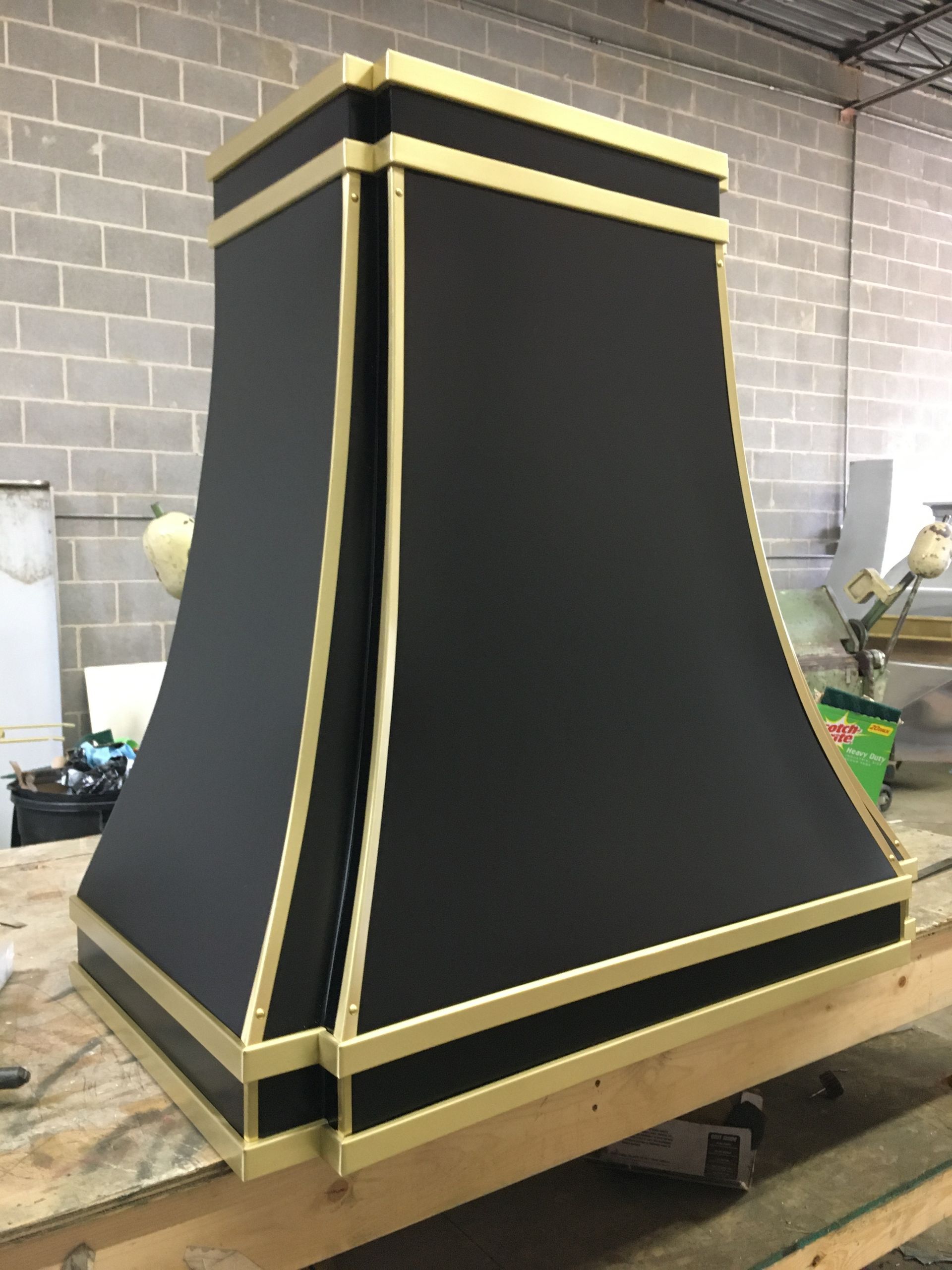 Black and gold decorative structure on a wooden pallet in a workshop, with a tapered, curved shape