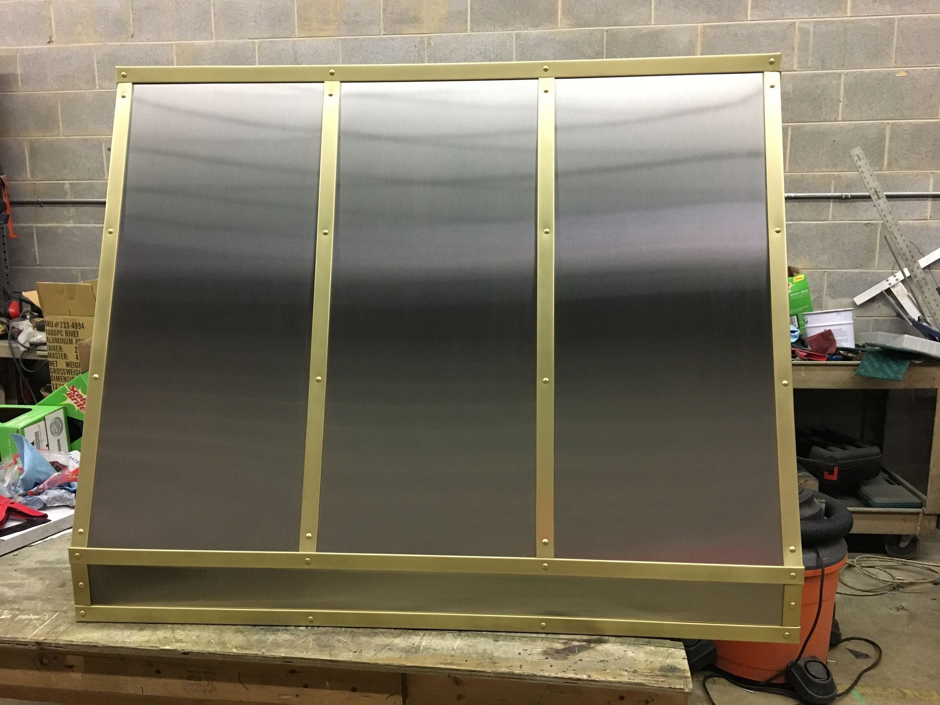 Large gold-framed reflective panel leaning in a workshop against a cinderblock wall