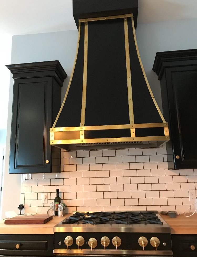Modern kitchen range with black-and-gold hood, white subway tile, and dark cabinets