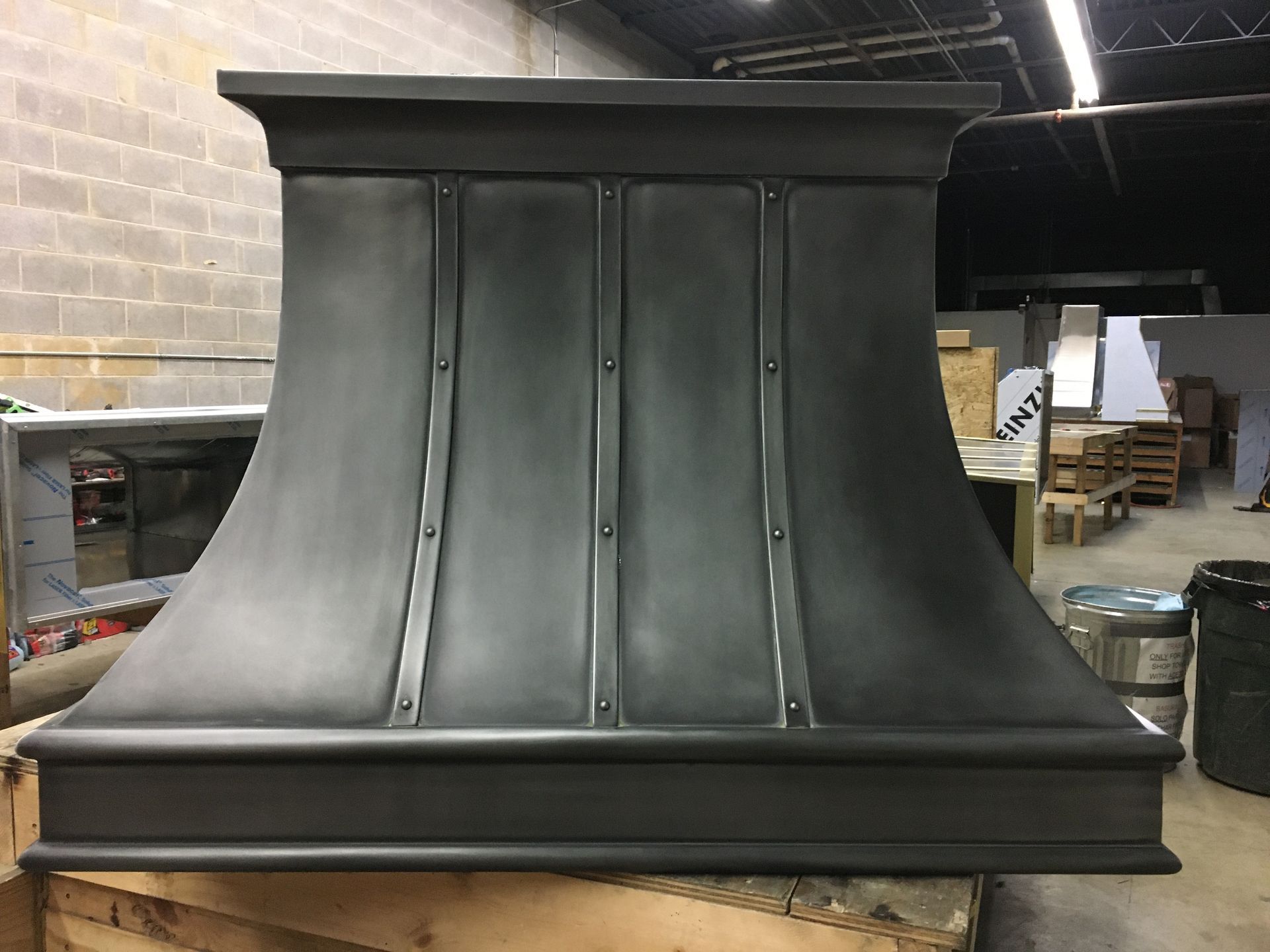 Black metal range hood in a workshop, with curved sides and a wide base.