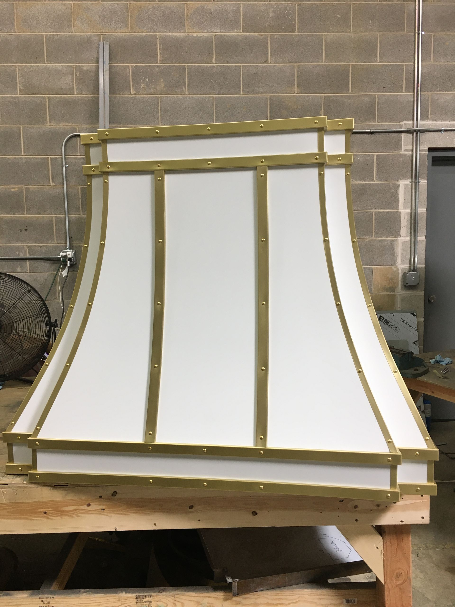 White curved panel with gold trim on a workbench in a workshop, against a cinderblock wall