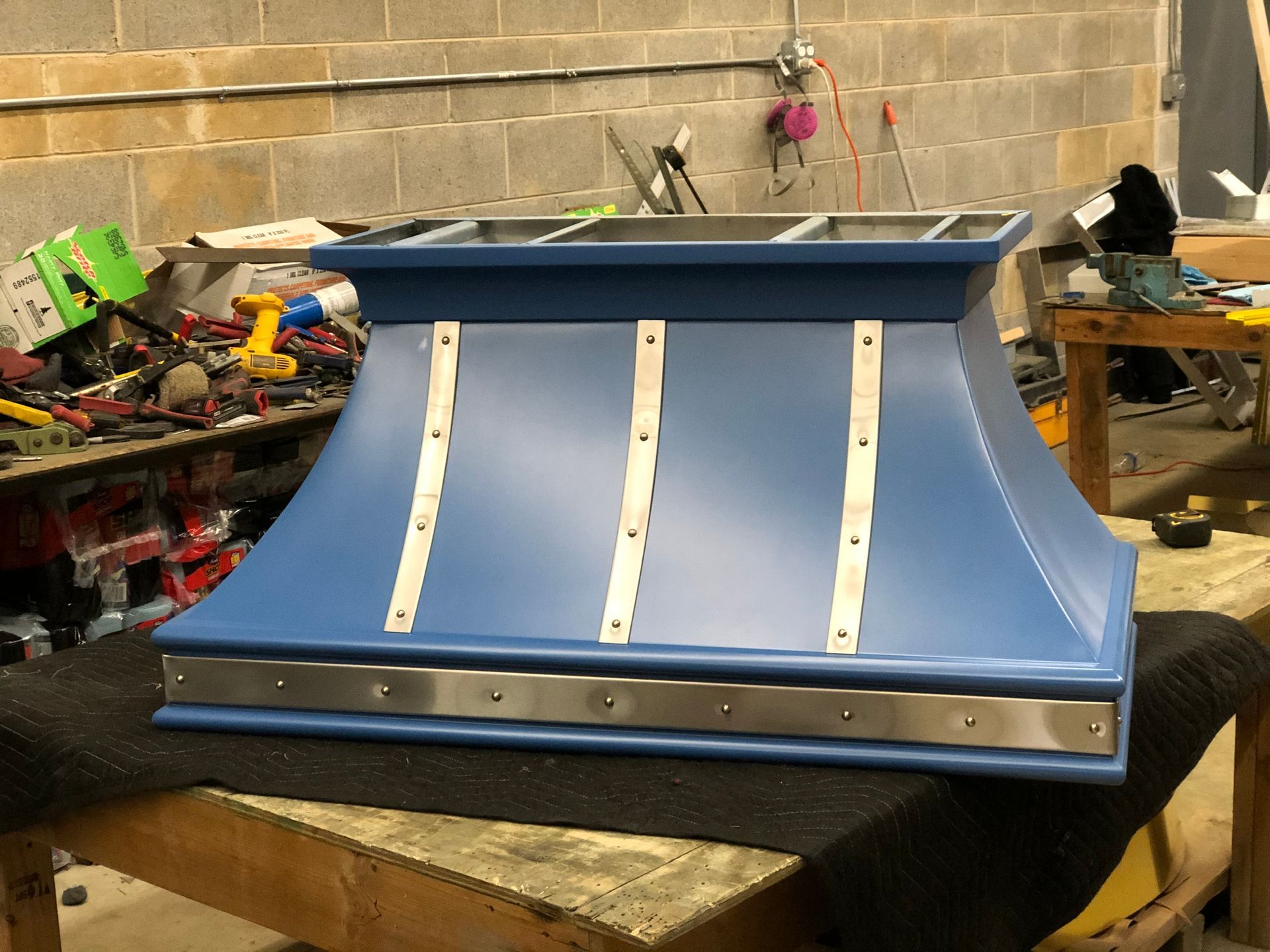 Blue metal snowplow blade in a workshop, with white support braces and tools on nearby tables