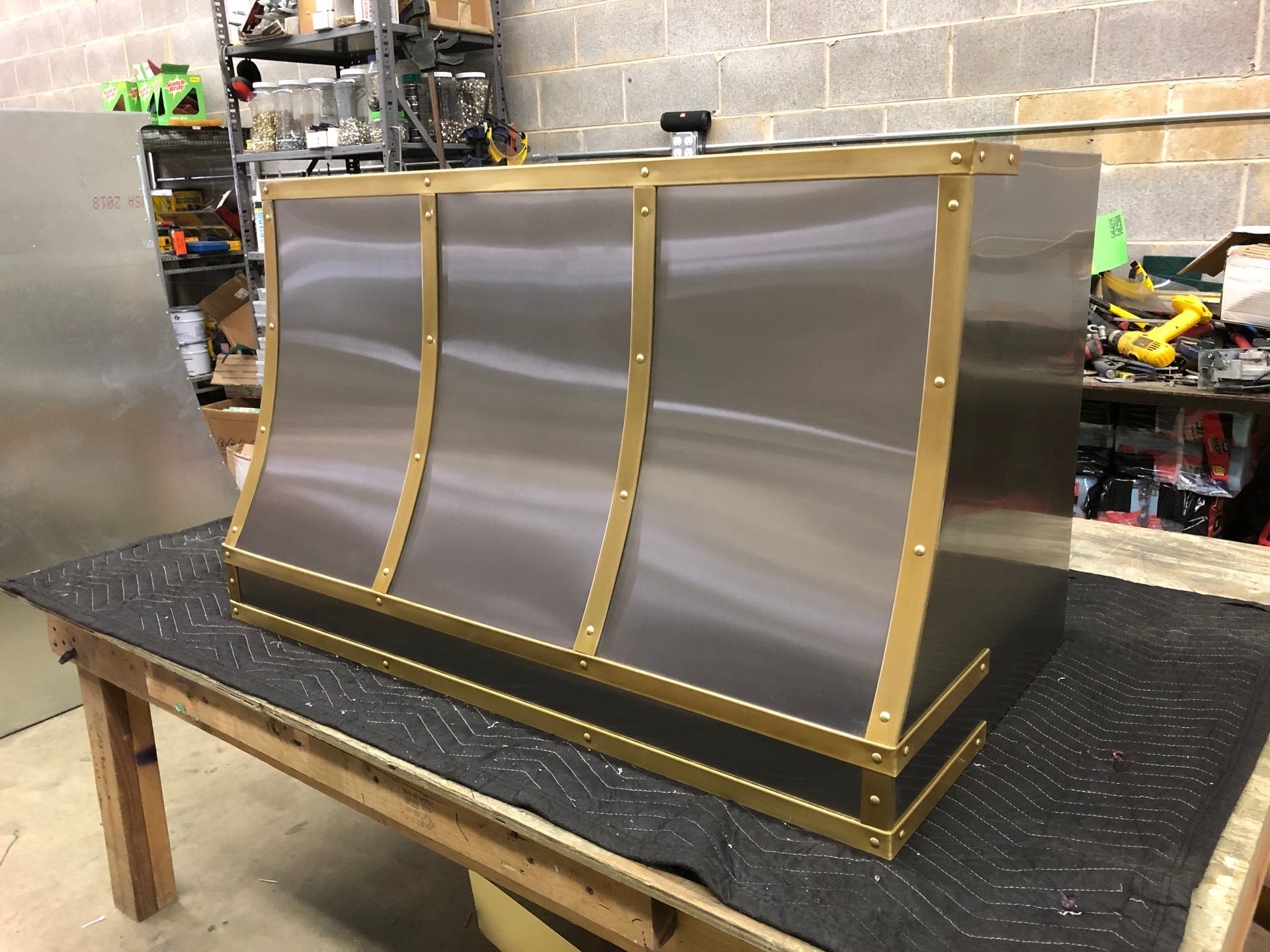 Curved metal panel with brass frame on a workbench in a workshop setting