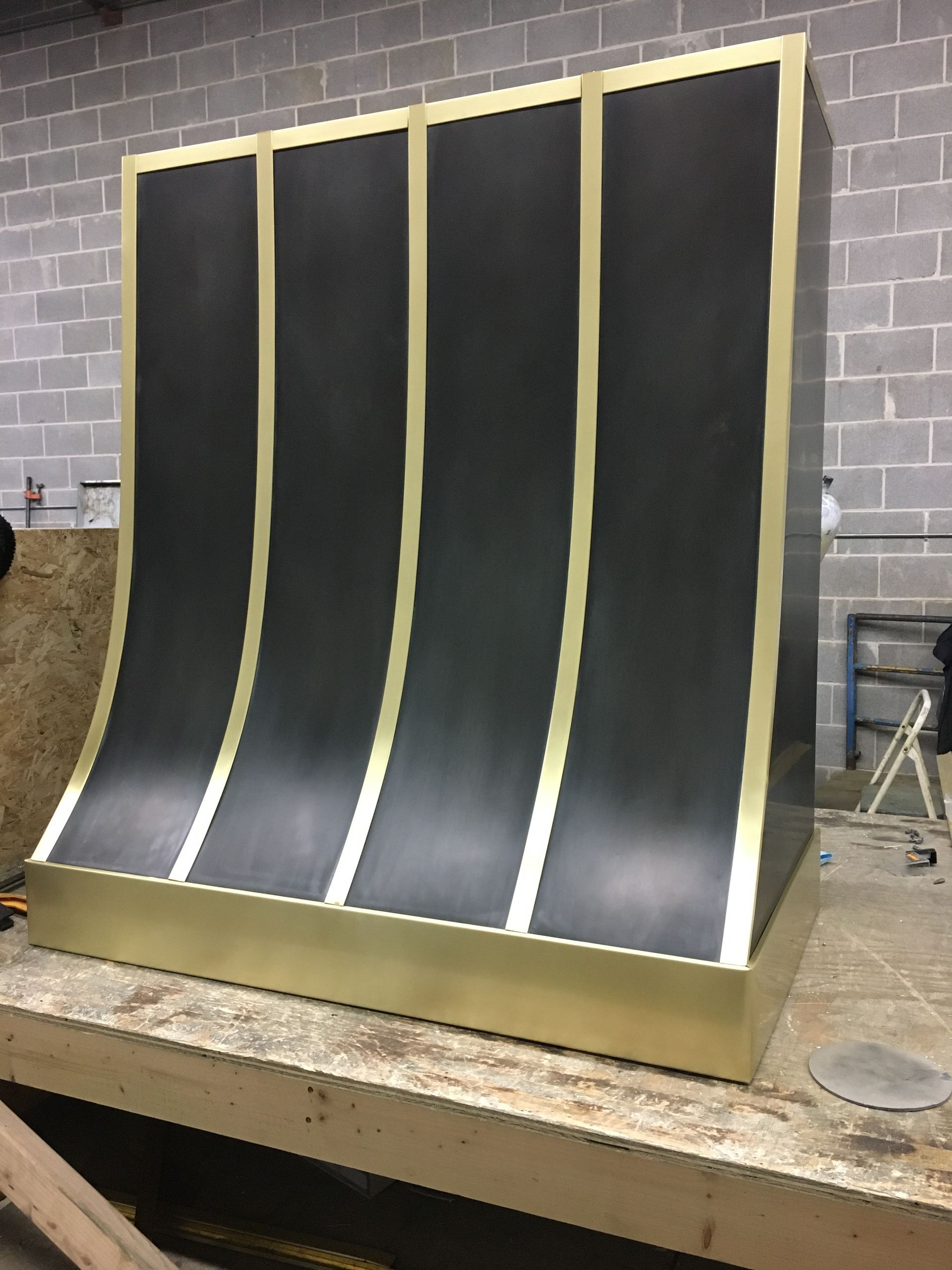 Black curved panel with gold trim on a workbench in a workshop with concrete block walls