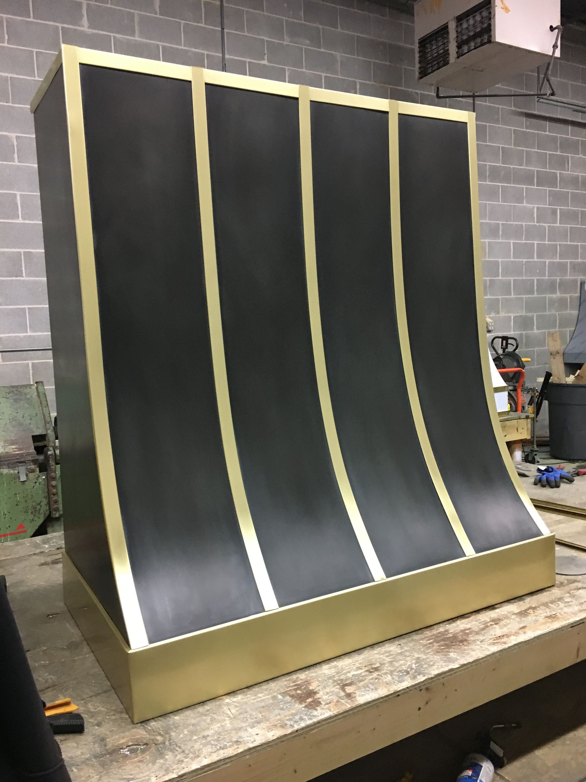 Curved black-and-gold metal panel display in a workshop with a brick wall background
