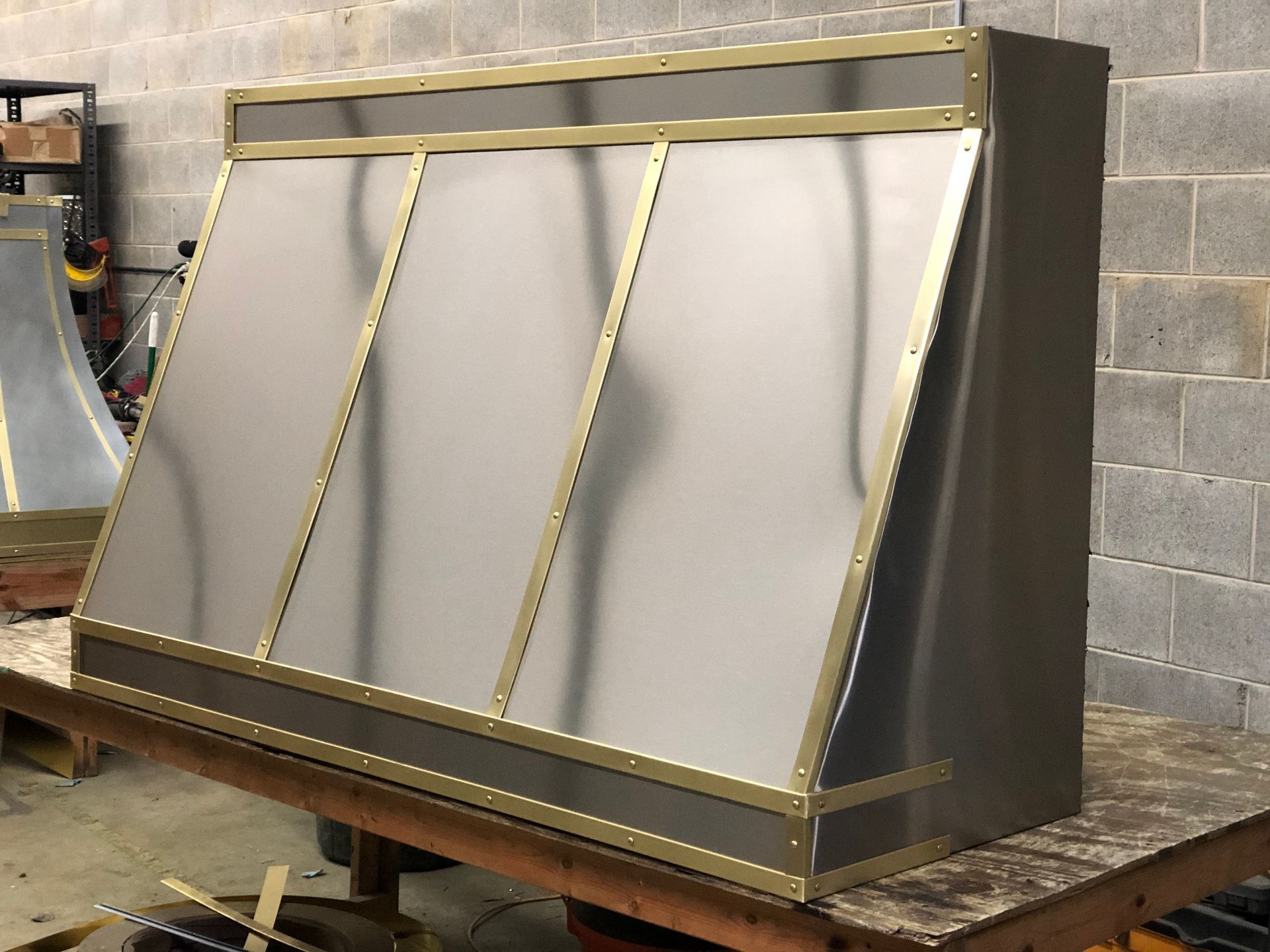 Metal industrial enclosure with angled gray panels and gold trim on a workbench in a workshop