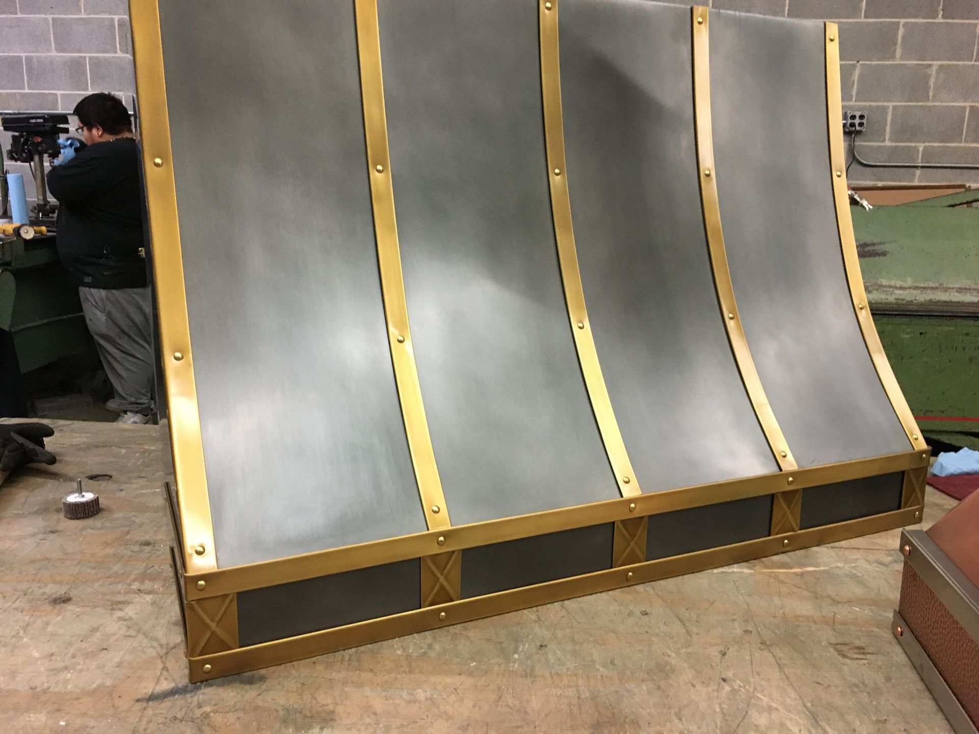 Large curved gray panels with gold trim arranged on a wooden frame outdoors near a wall