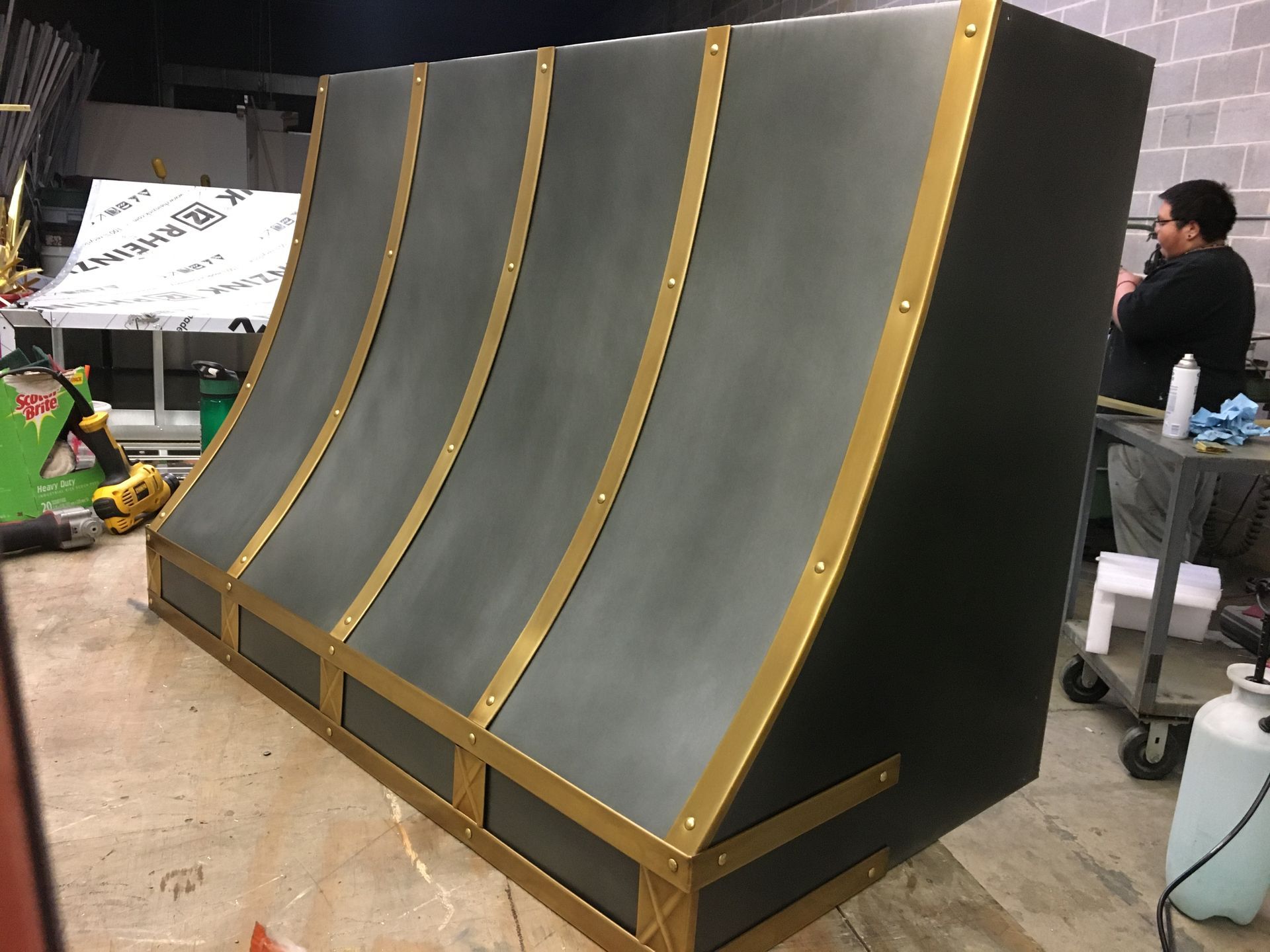 Large black-and-gold curved ramp structure in a workshop or studio, with people and equipment in the background