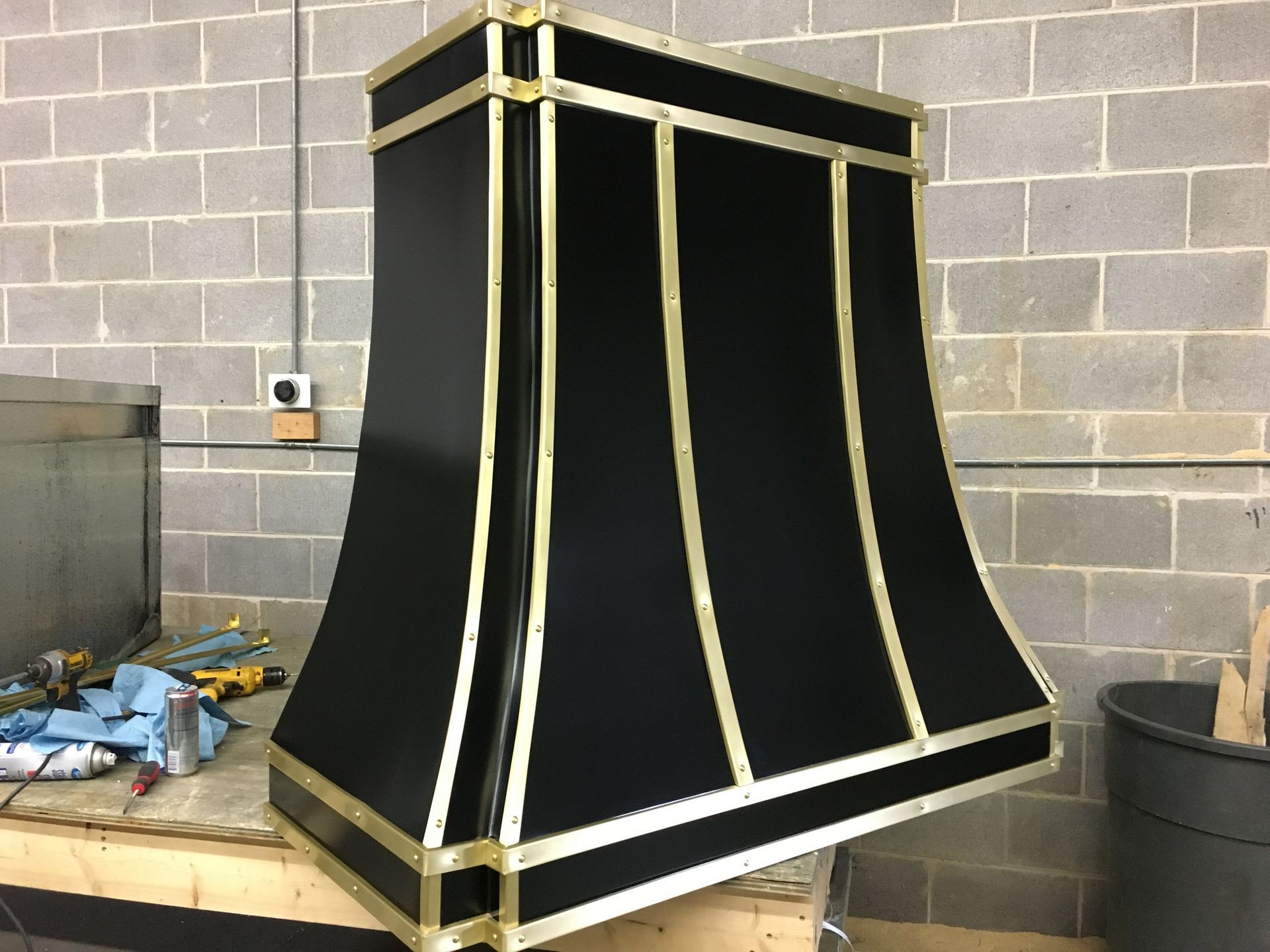 Large black-and-gold metal hood or cabinet in an industrial workshop against a cinderblock wall