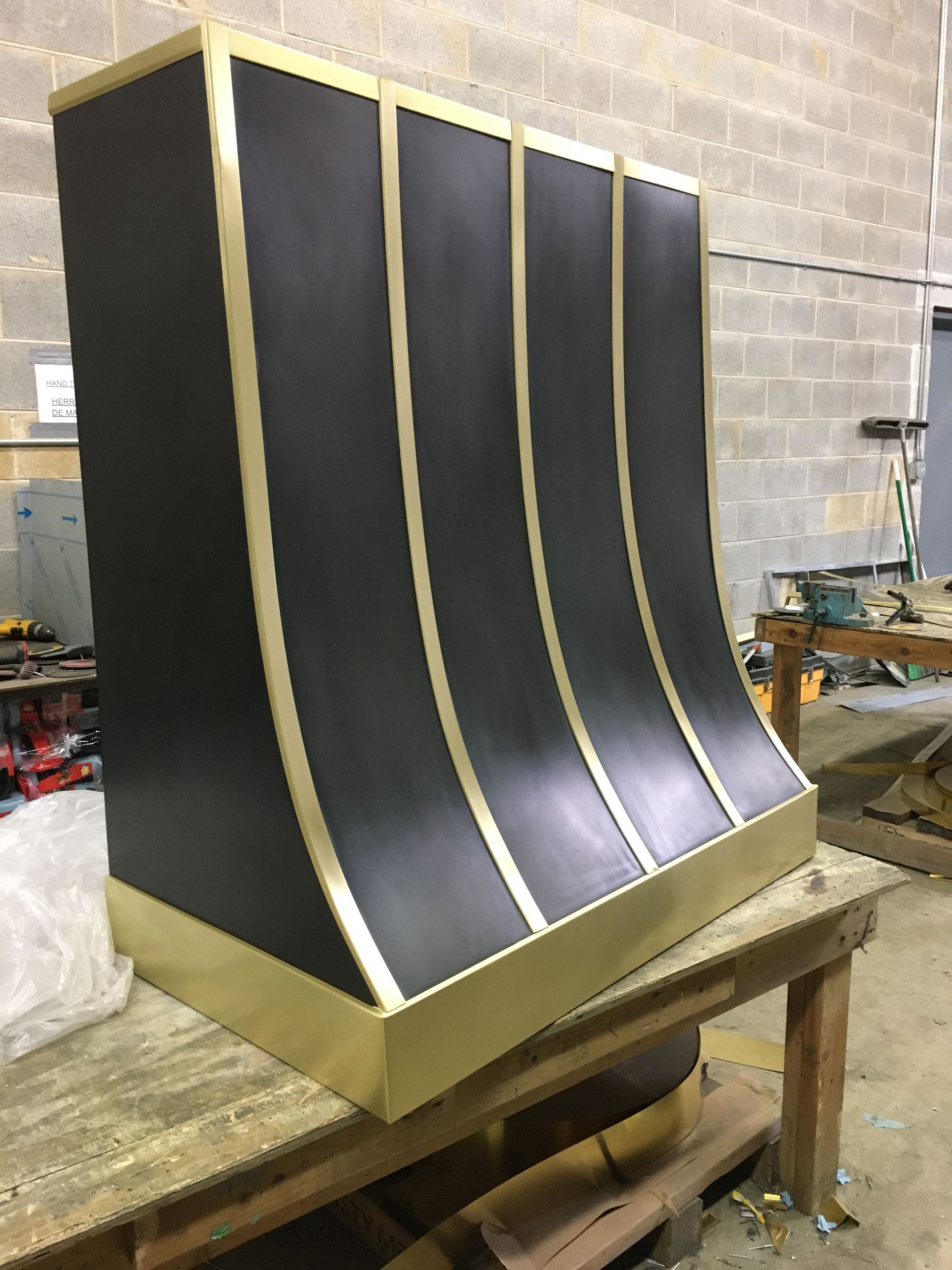 Curved black-and-gold metal panel on a workbench in a workshop