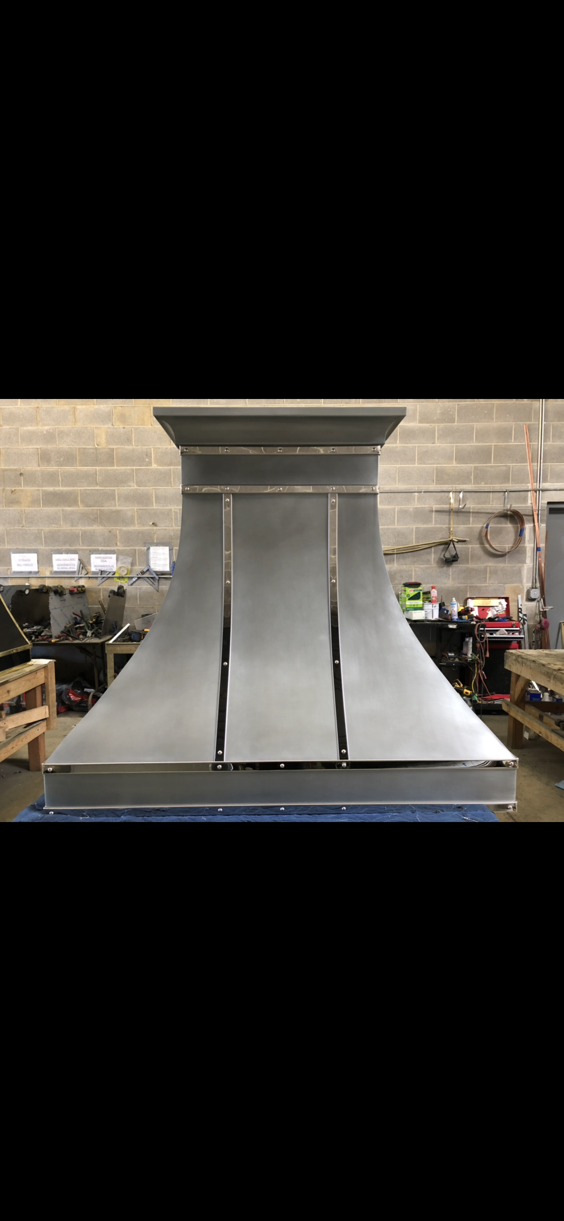 Industrial metal hood with a wide base in a workshop, shown front-on against a brick wall