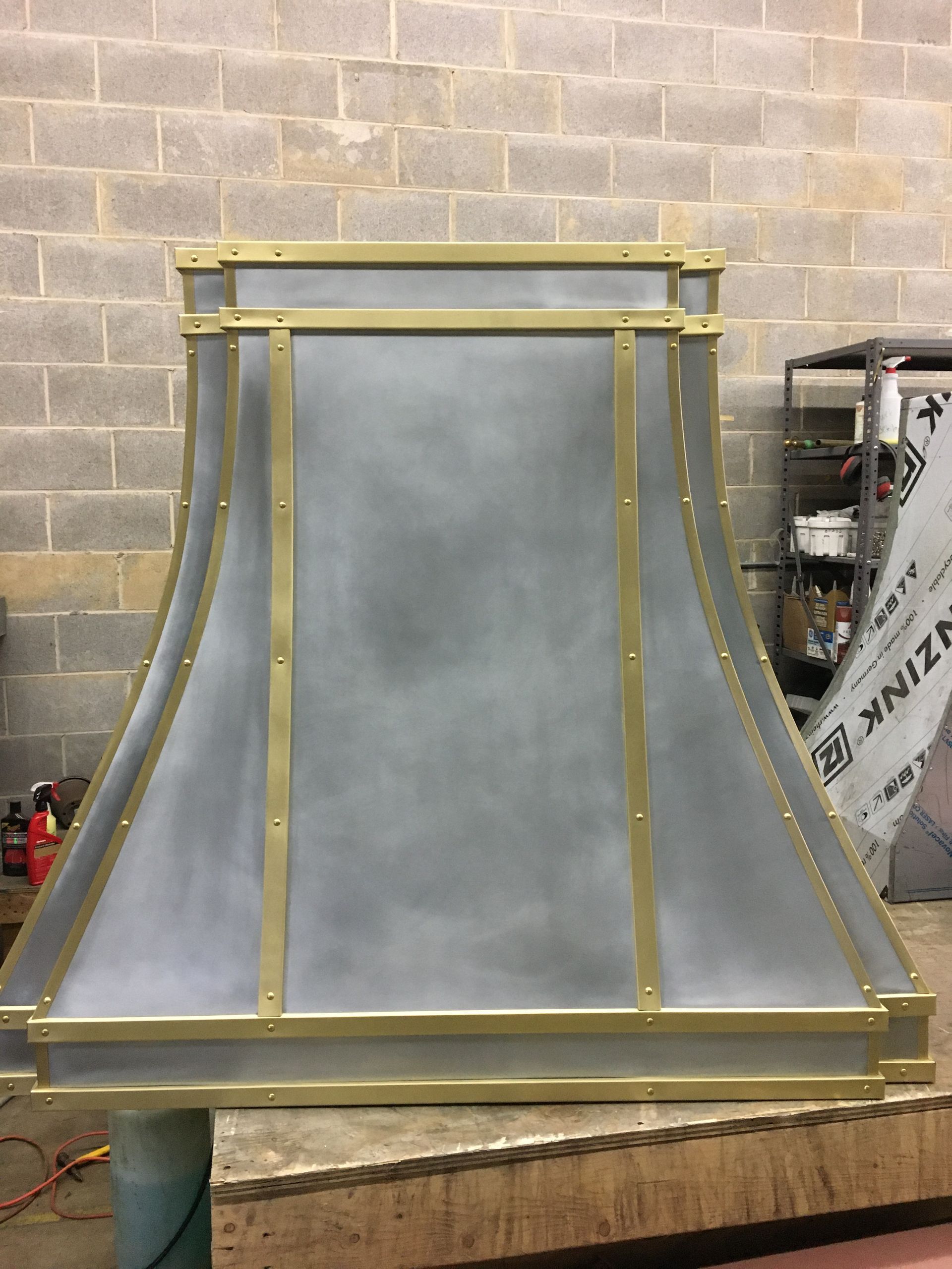 Metal duct hood with gold trim in a workshop against a cinderblock wall