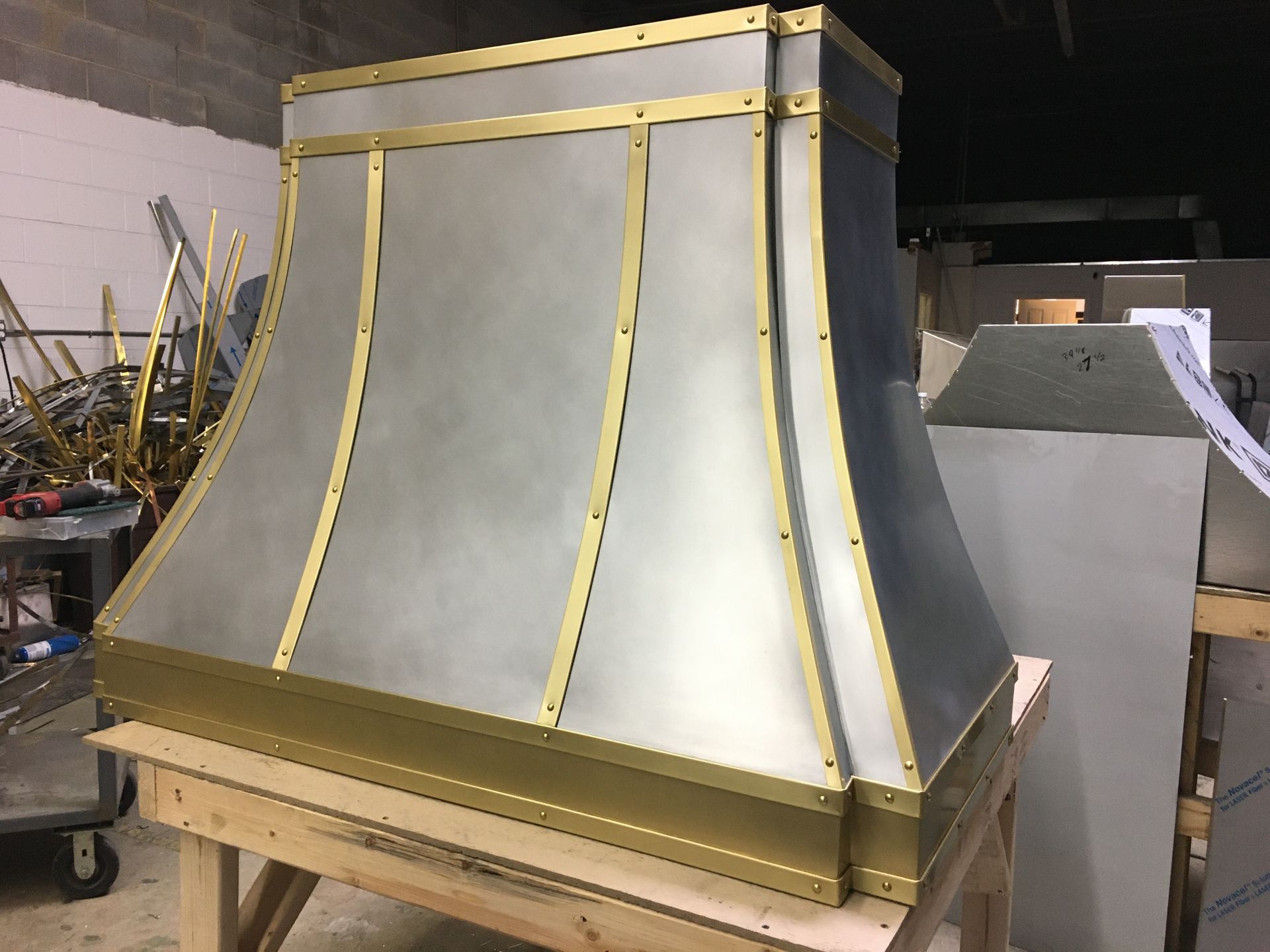 Large unfinished decorative metal structure with gray panels and gold trim on a wooden cart in a workshop.