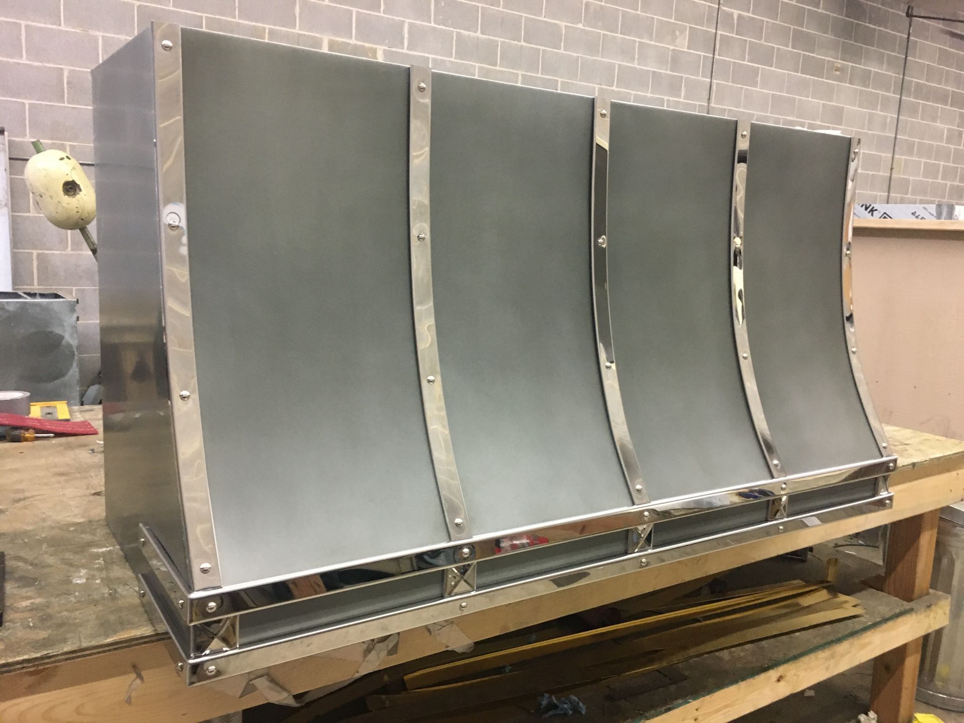 Four curved metal panels mounted on a wooden frame in a workshop setting