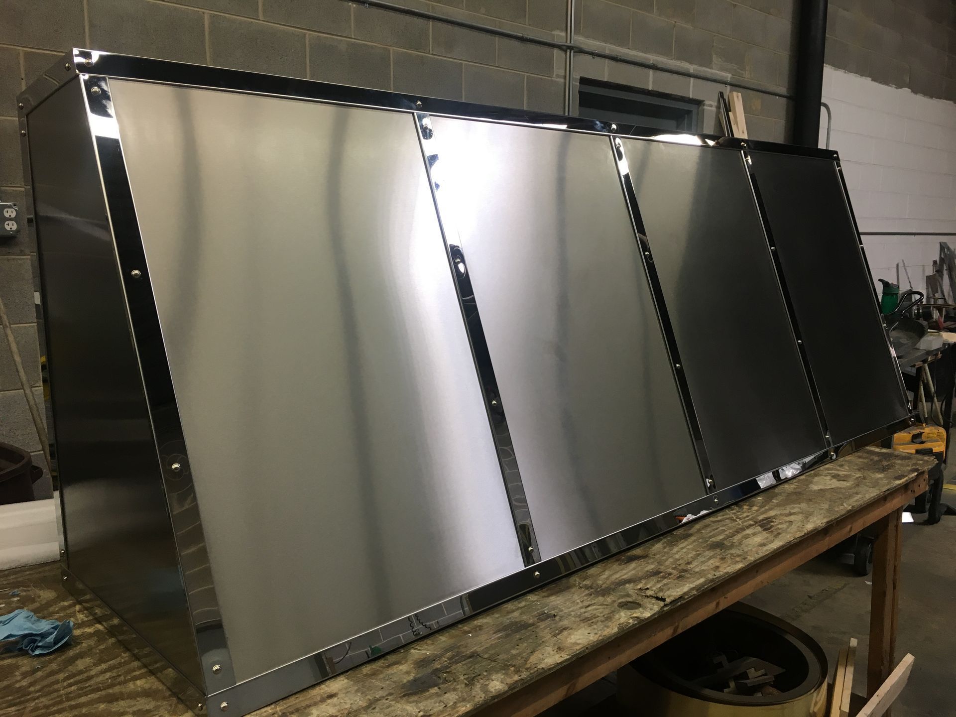 Four large reflective metal panels leaning on a wooden workbench in a workshop