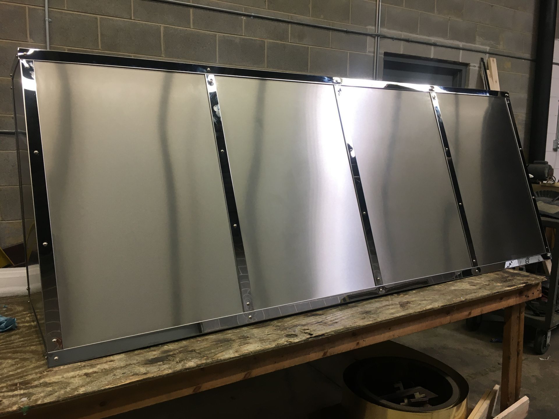 Five reflective metal panels leaned on a workbench in a workshop.