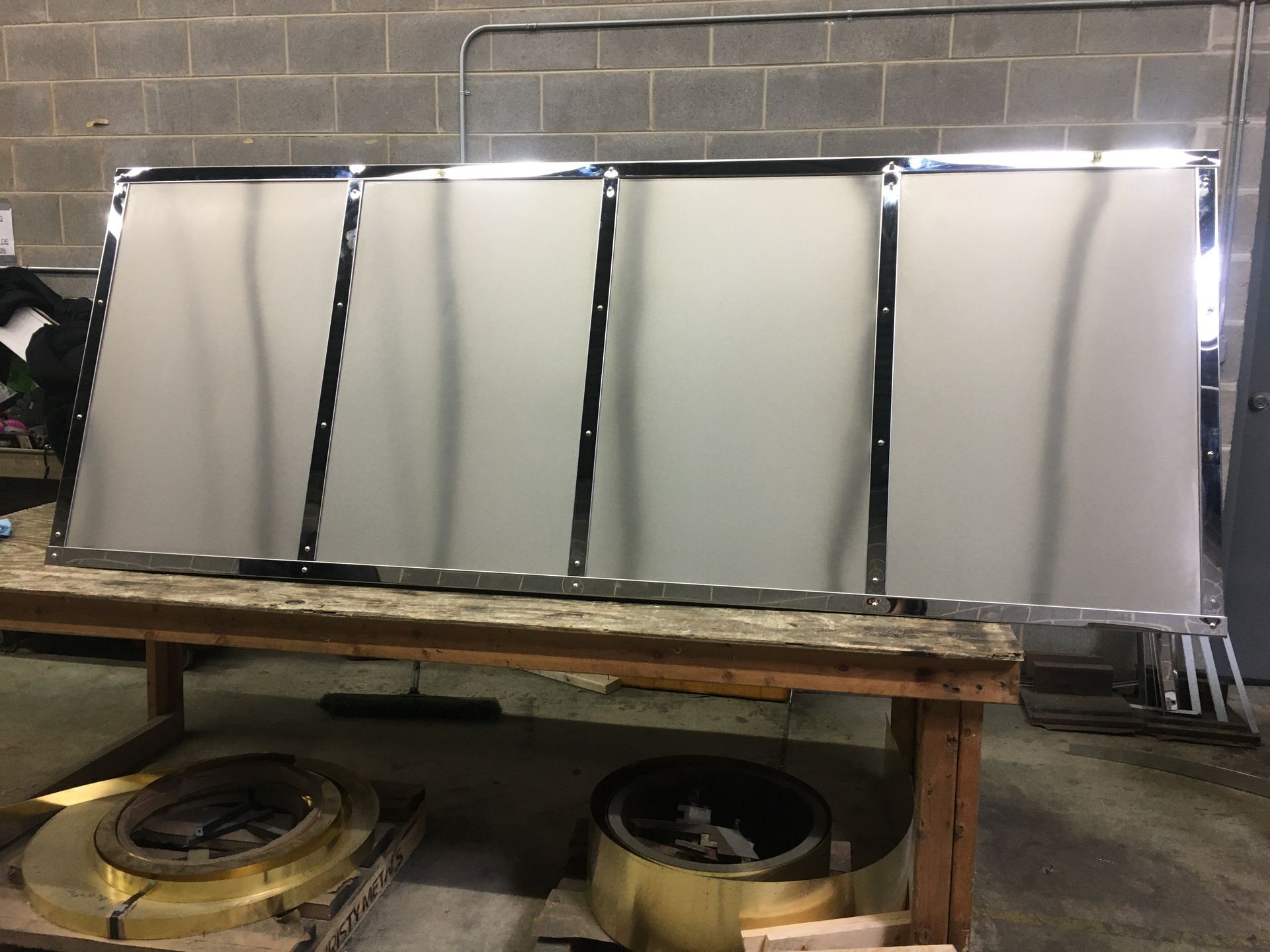 Four large silver metal panels leaning on a wooden bench in an industrial workshop.