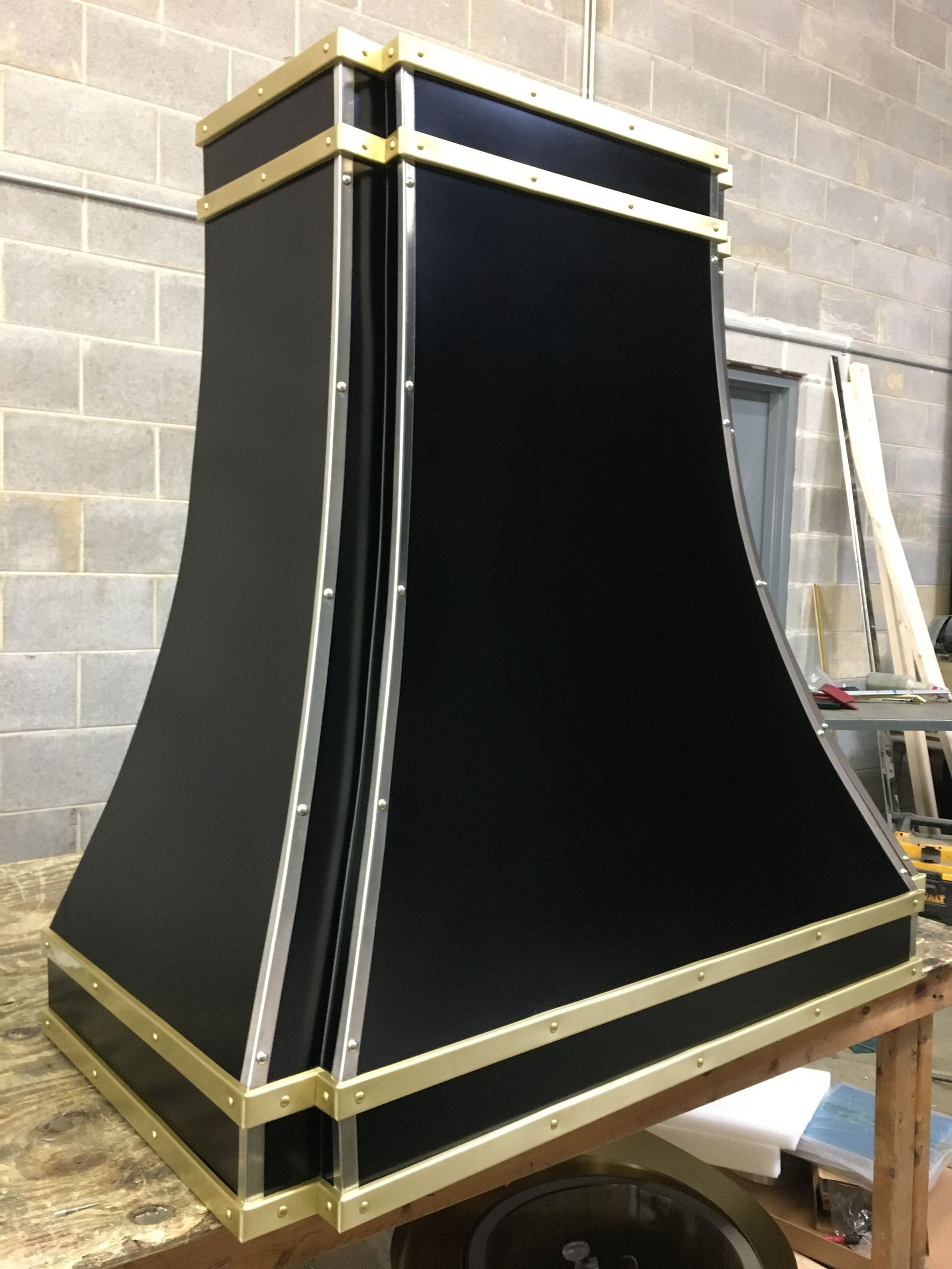 Black and gold decorative cabinet or display case with flared sides against a brick wall