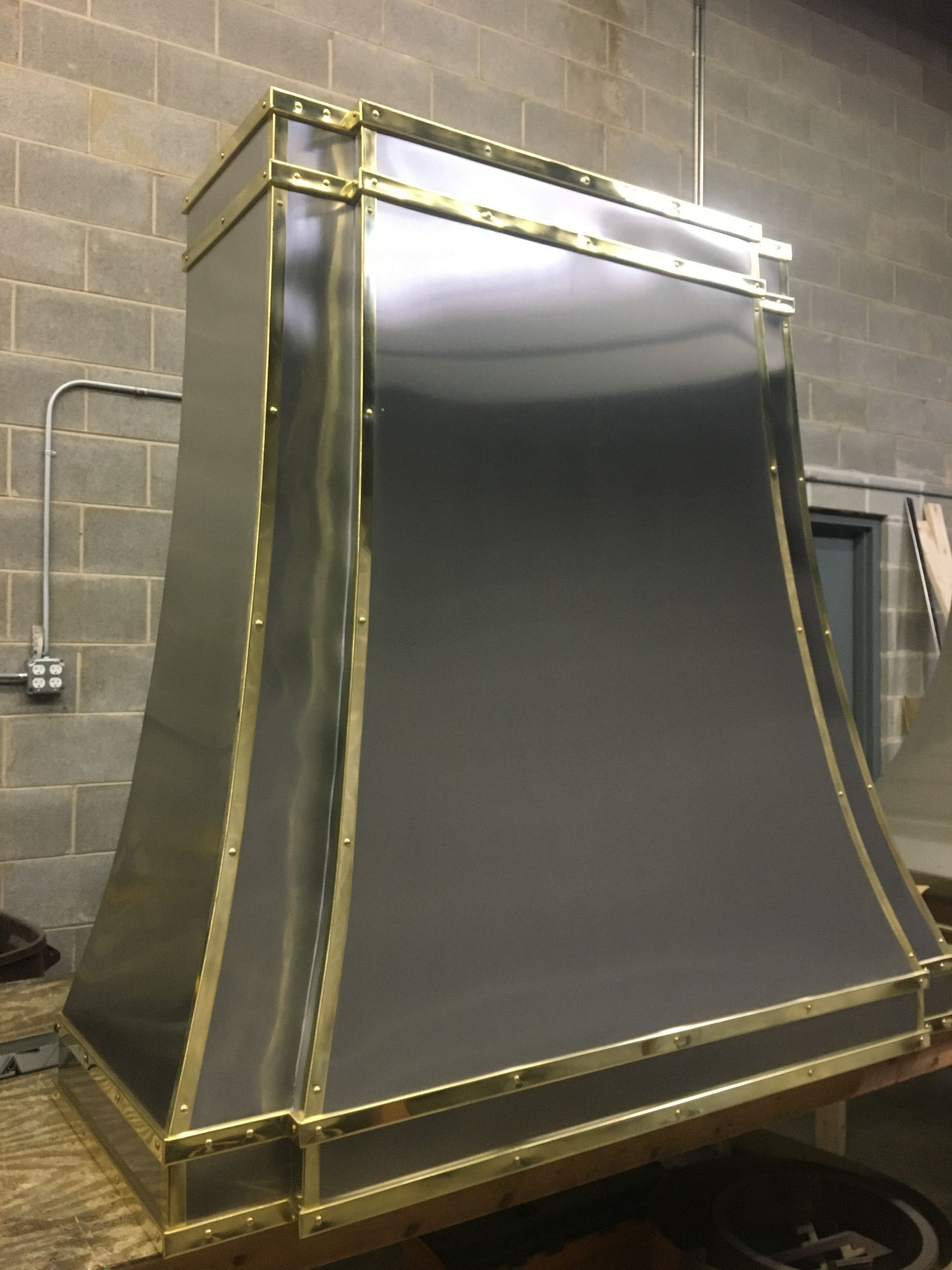 Large brass-trimmed metal hood or enclosure in a workshop, with a dark front panel and sloped sides