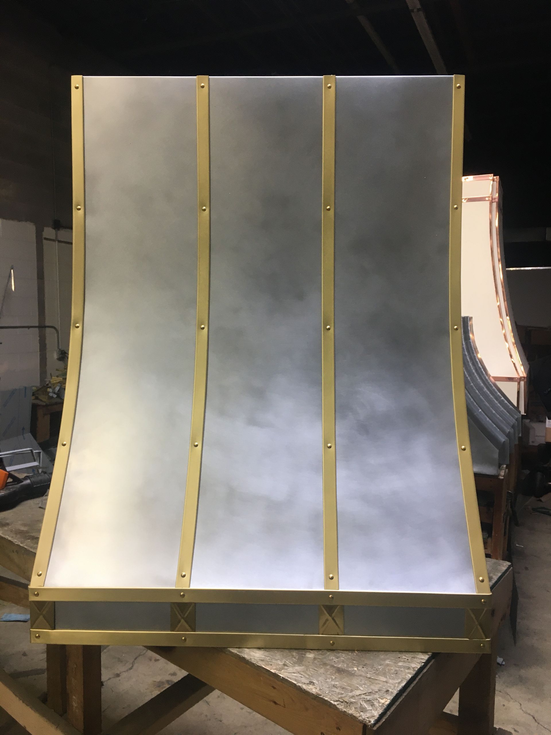 Curved silver metal ramp or slide with gold vertical supports in a workshop.